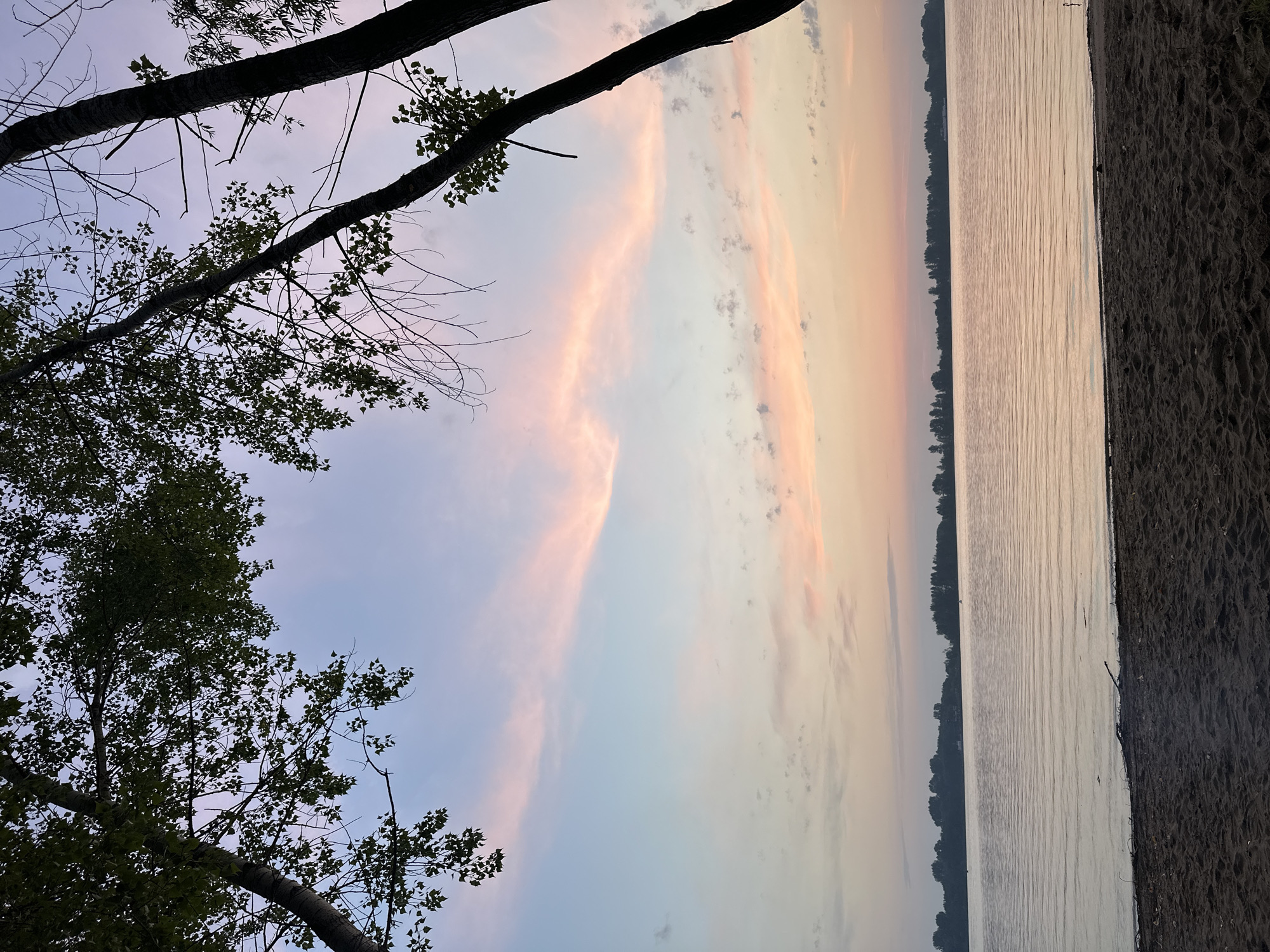 Lakeside beach at sunset, soft sky and still water.