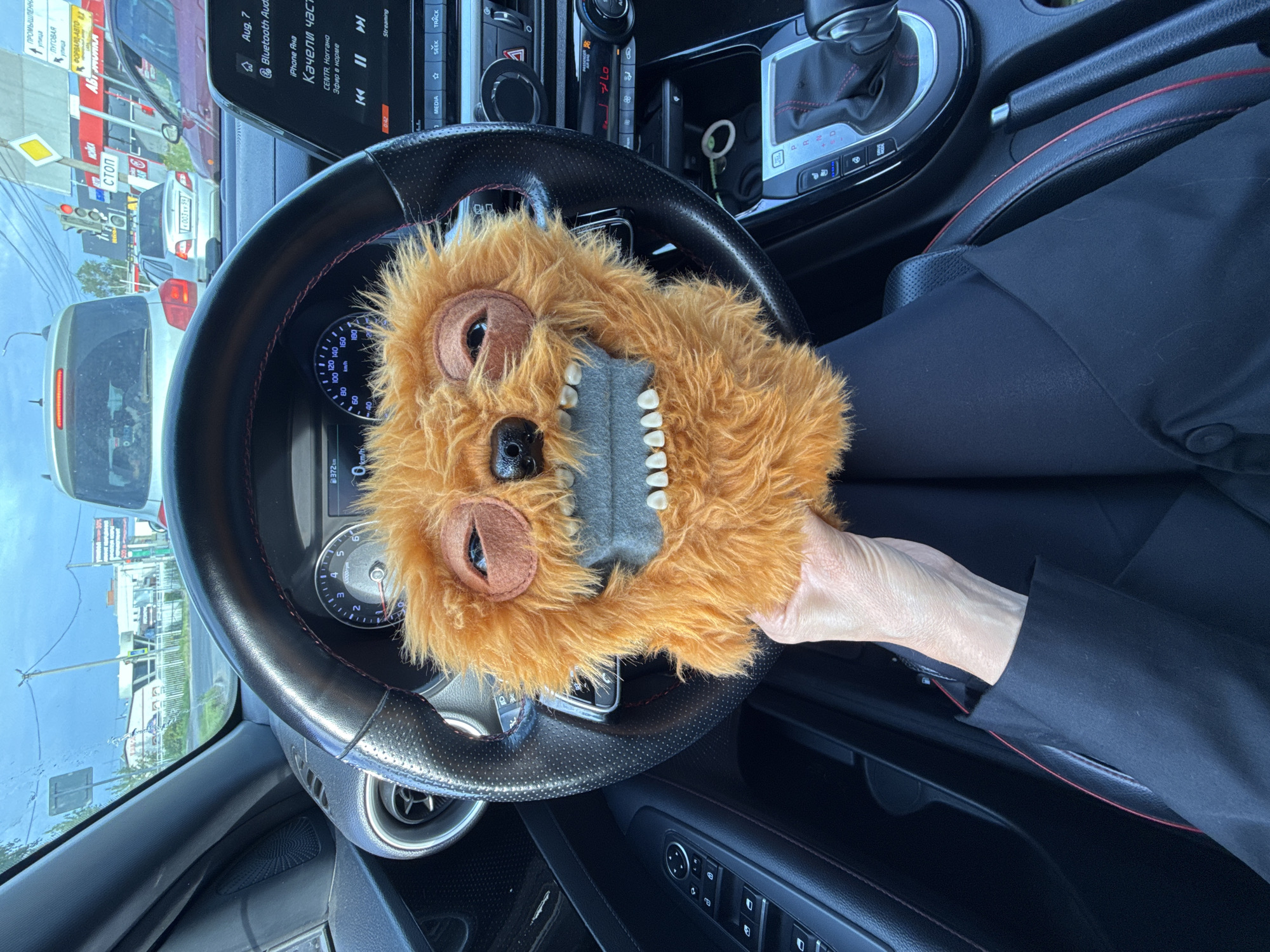 Fuzzy orange toy monster posed at the steering wheel in Chaikovsky