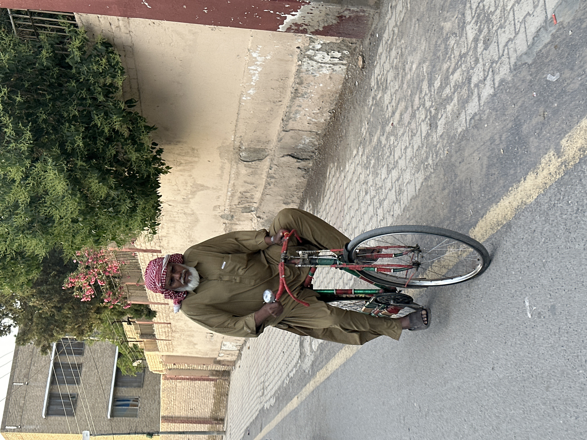 Elderly man stands on bicycle in Quetta street