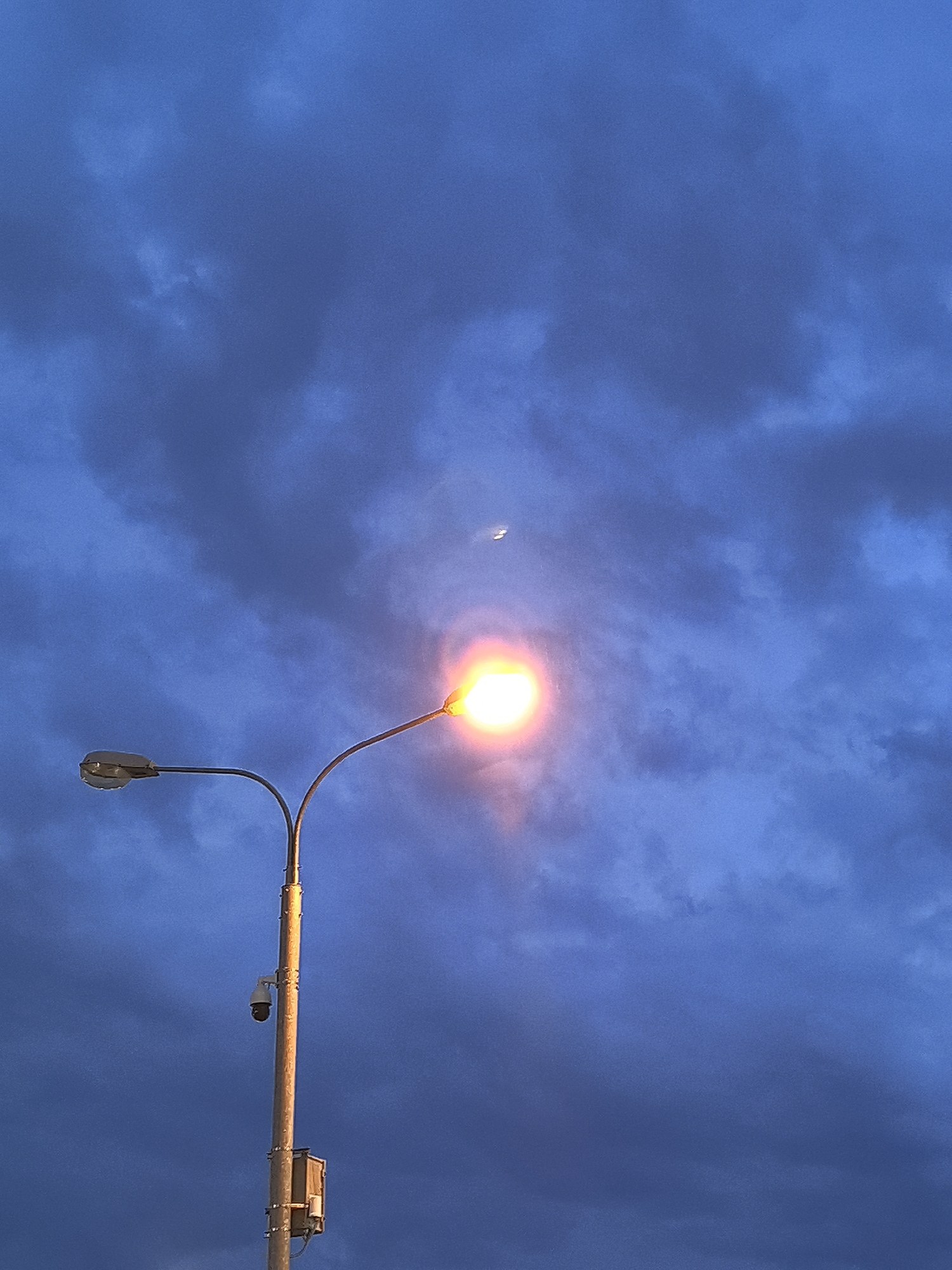 Streetlamp and crescent moon share a cloudy night sky