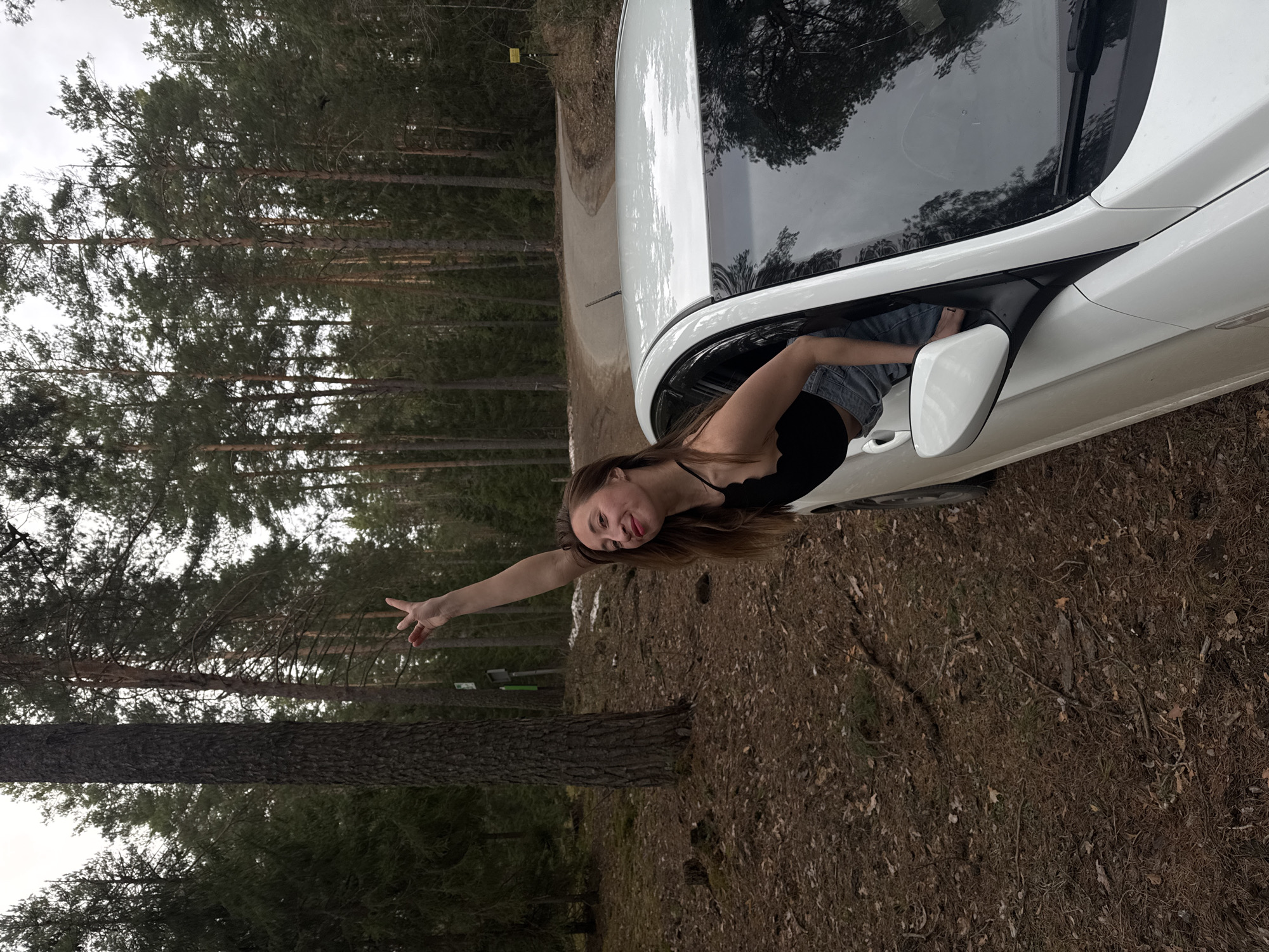 Woman poses playfully in car window during forest photoshoot