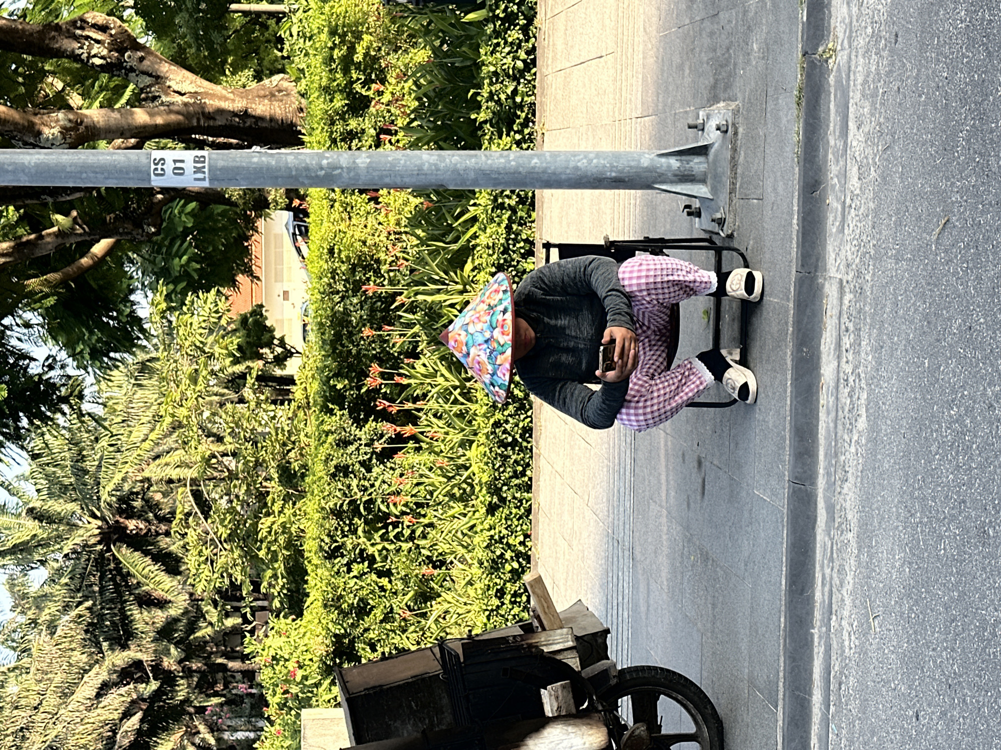 Elderly man in traditional hat uses phone on Đà Nẵng sidewalk