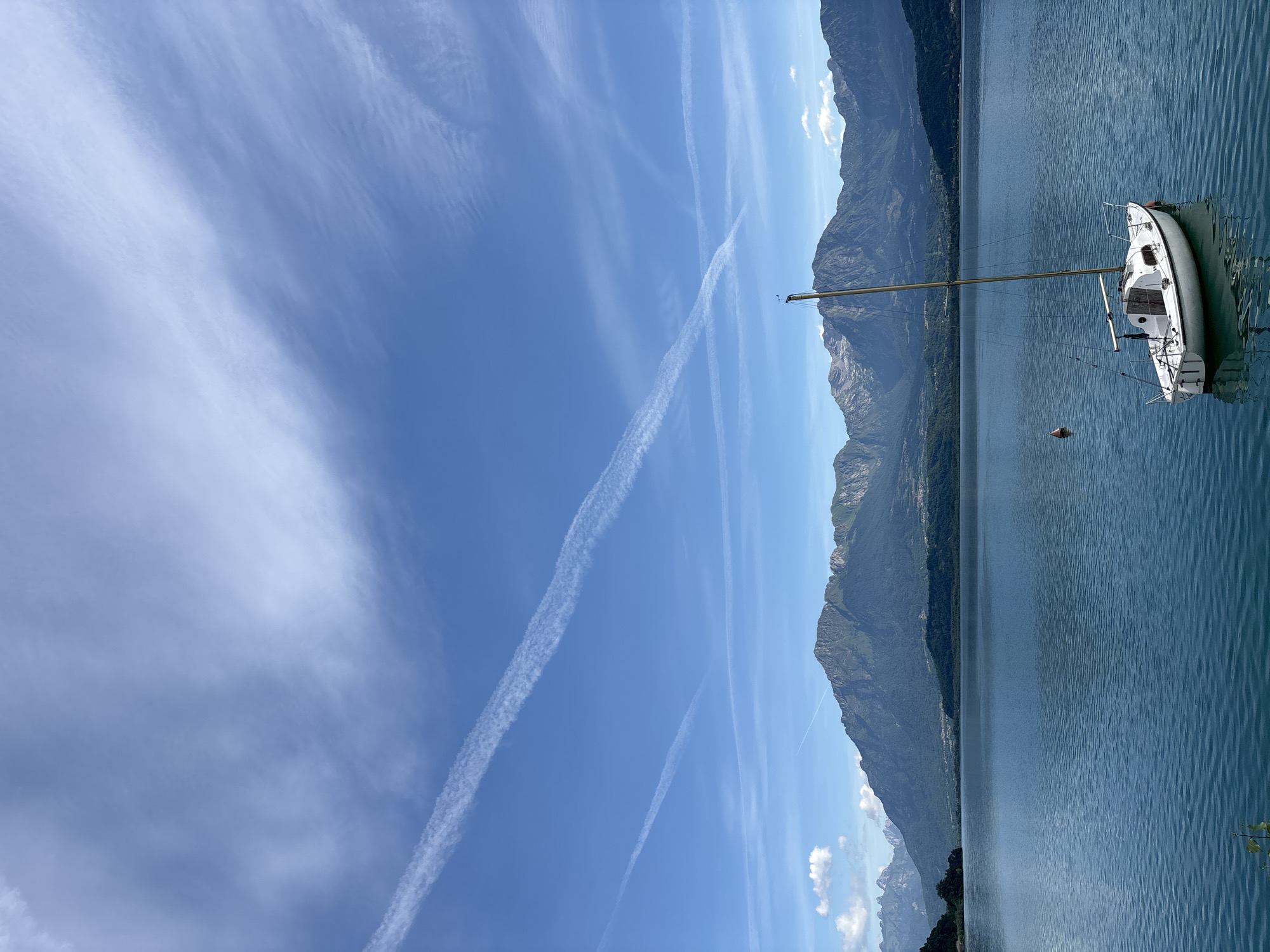 White sailboat moored on calm Italian lake near red buoy