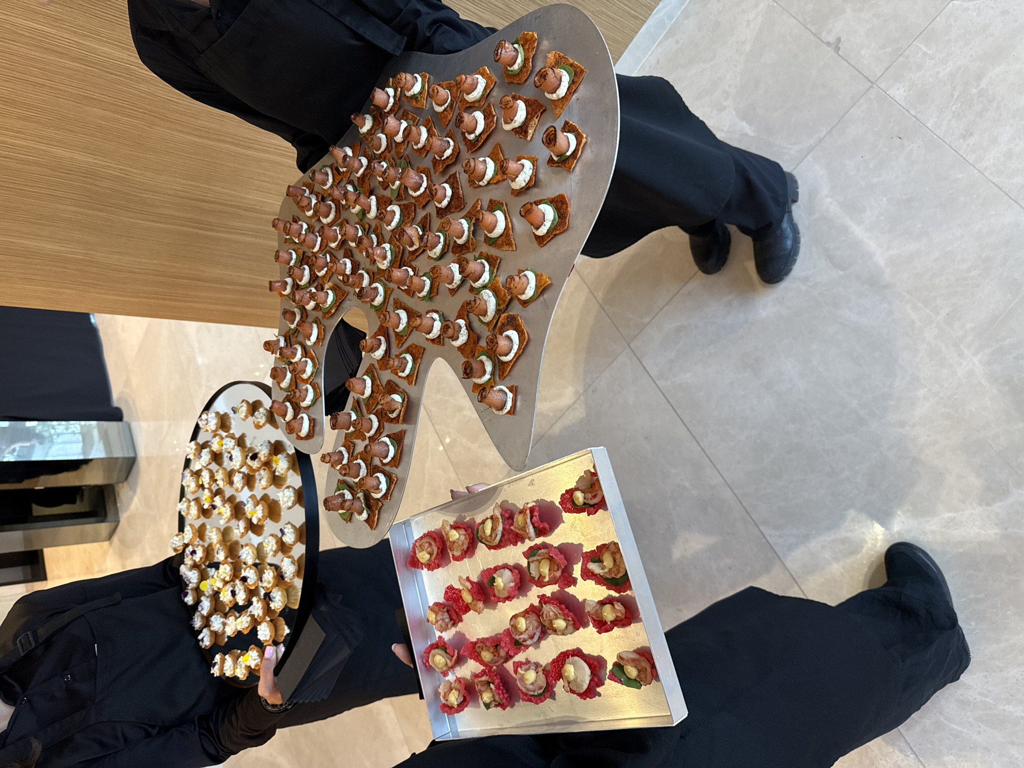 Two servers hold appetizer trays on marble floor
