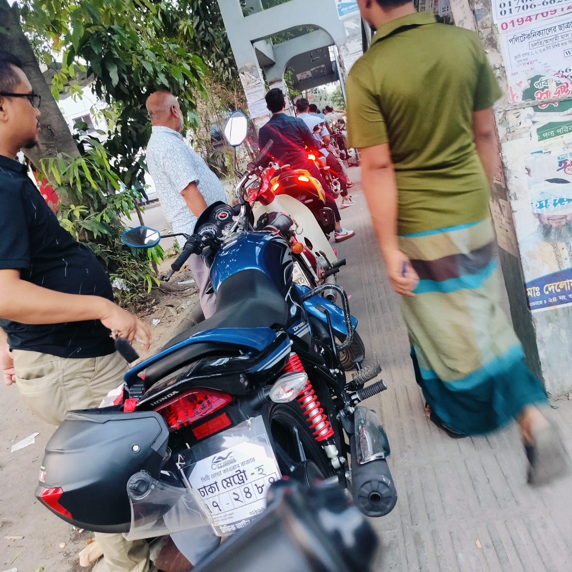 Motorcycles parked on Dhaka street with people gathering nearby