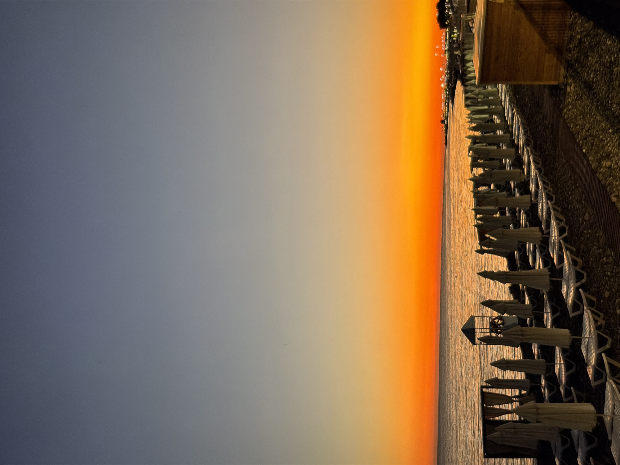 Sunset on a rocky beach, ending at a lit-up café