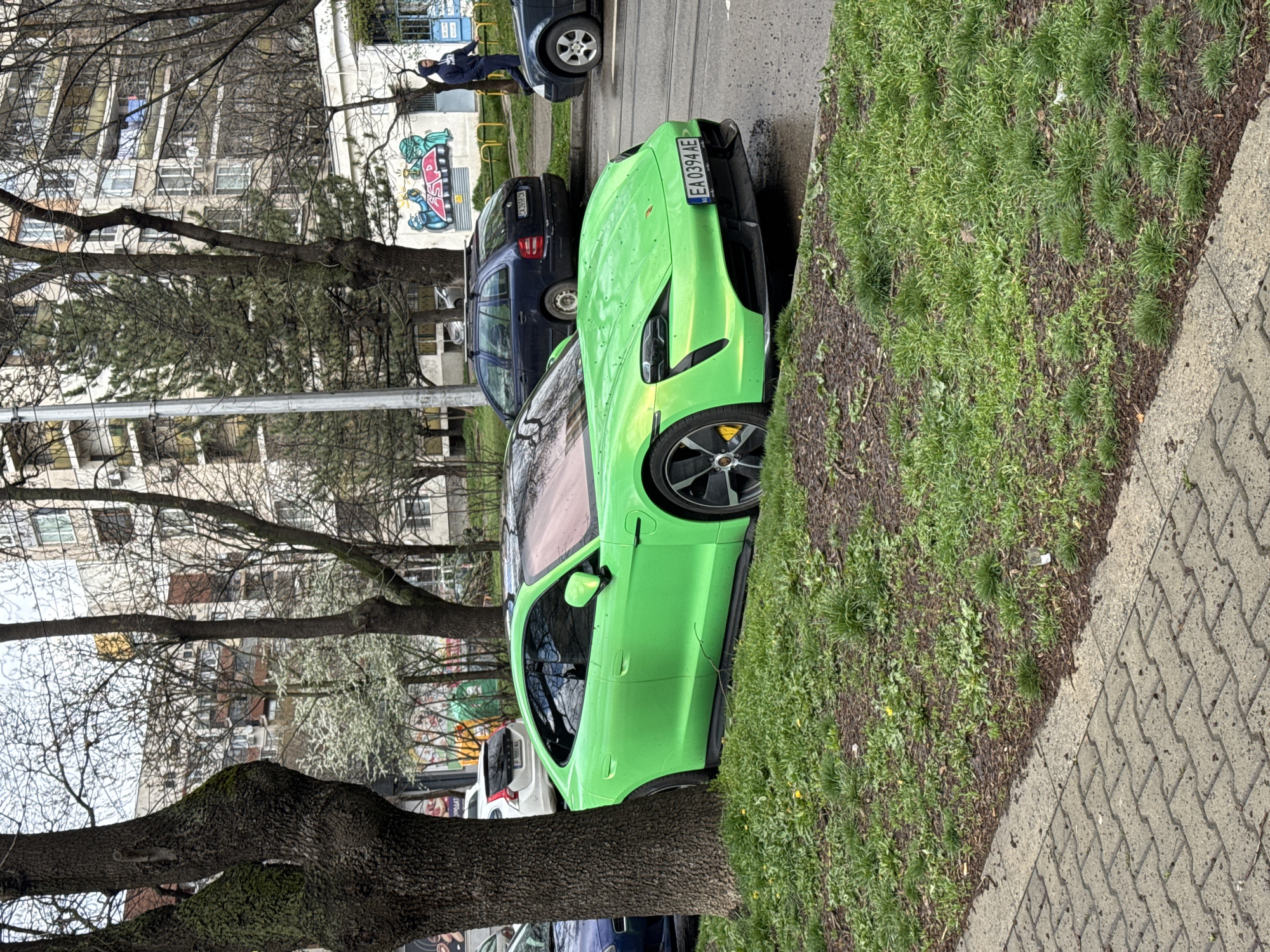 Green car parked near sidewalk, person by graffitied building