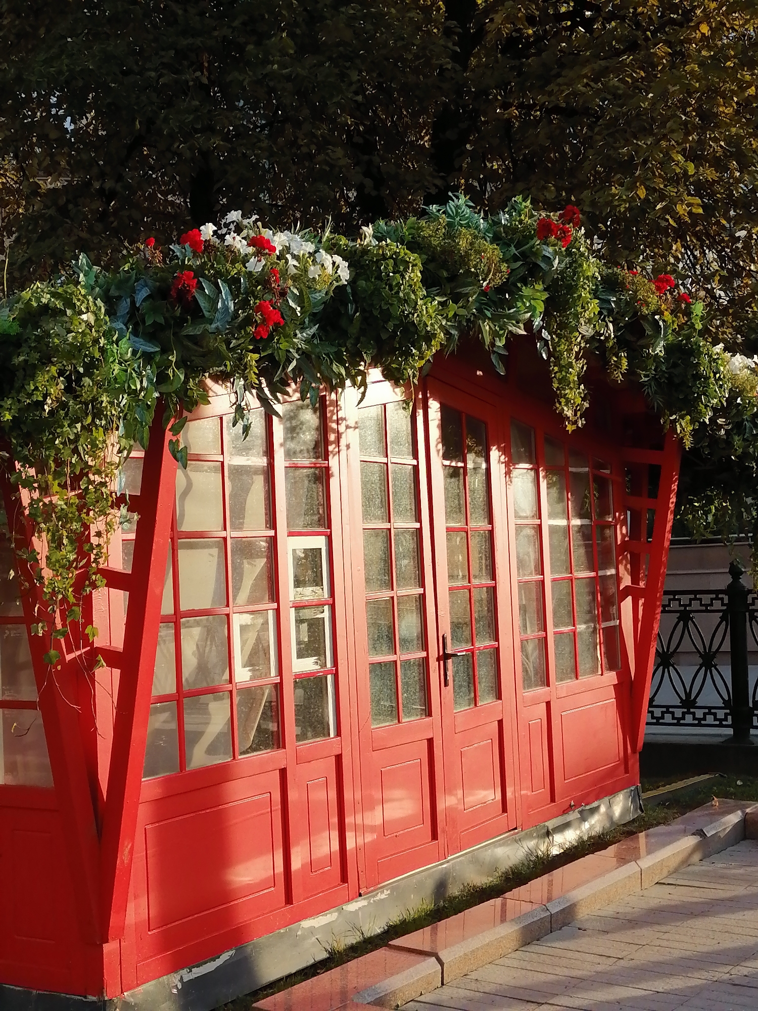 Red greenhouse structure dressed up with roofline flowers and greenery