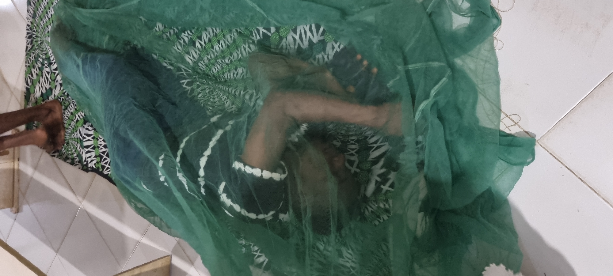 Resting under a green mosquito net indoors in Lagos