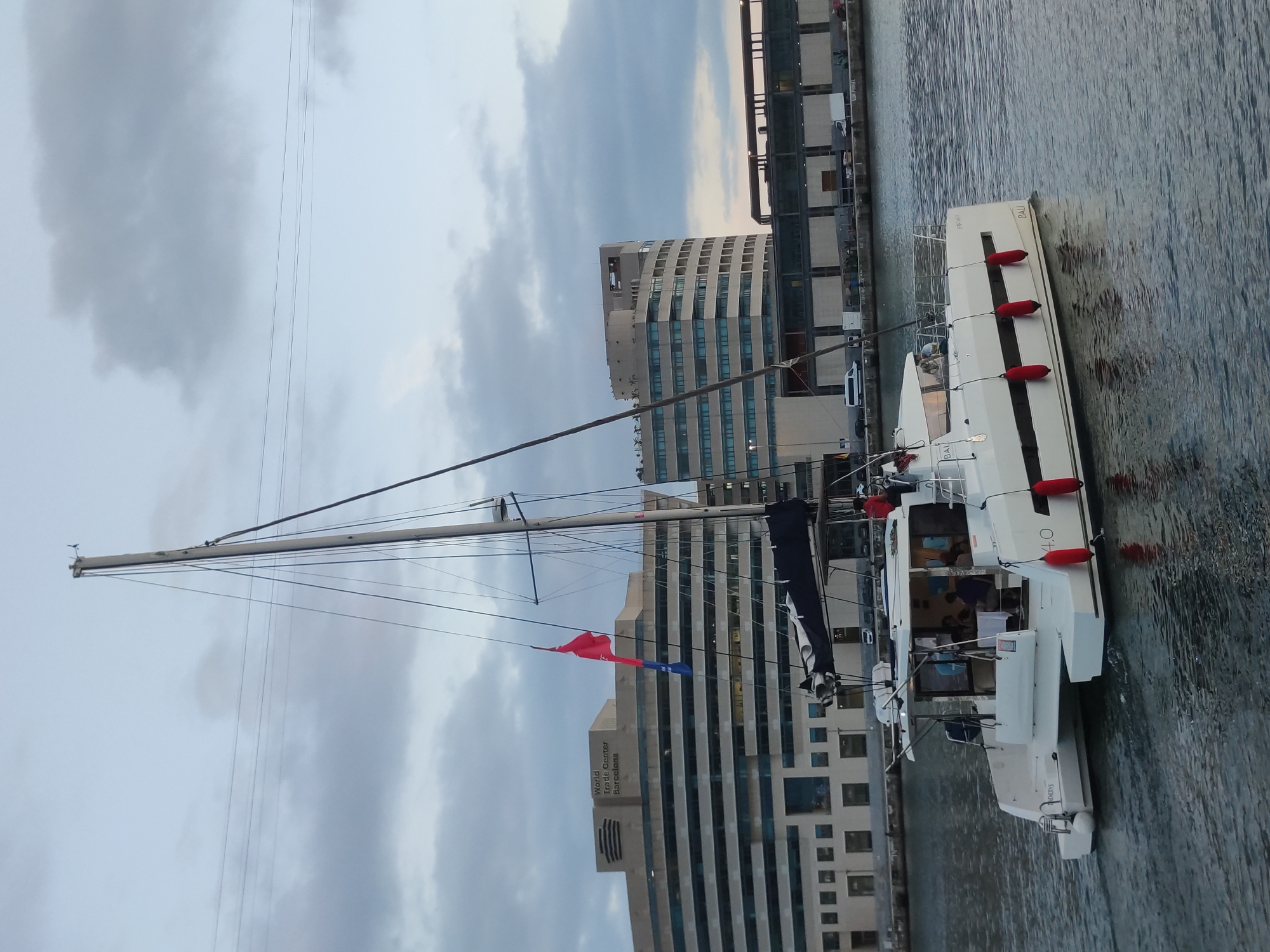 White catamaran sails Barcelona harbor at twilight
