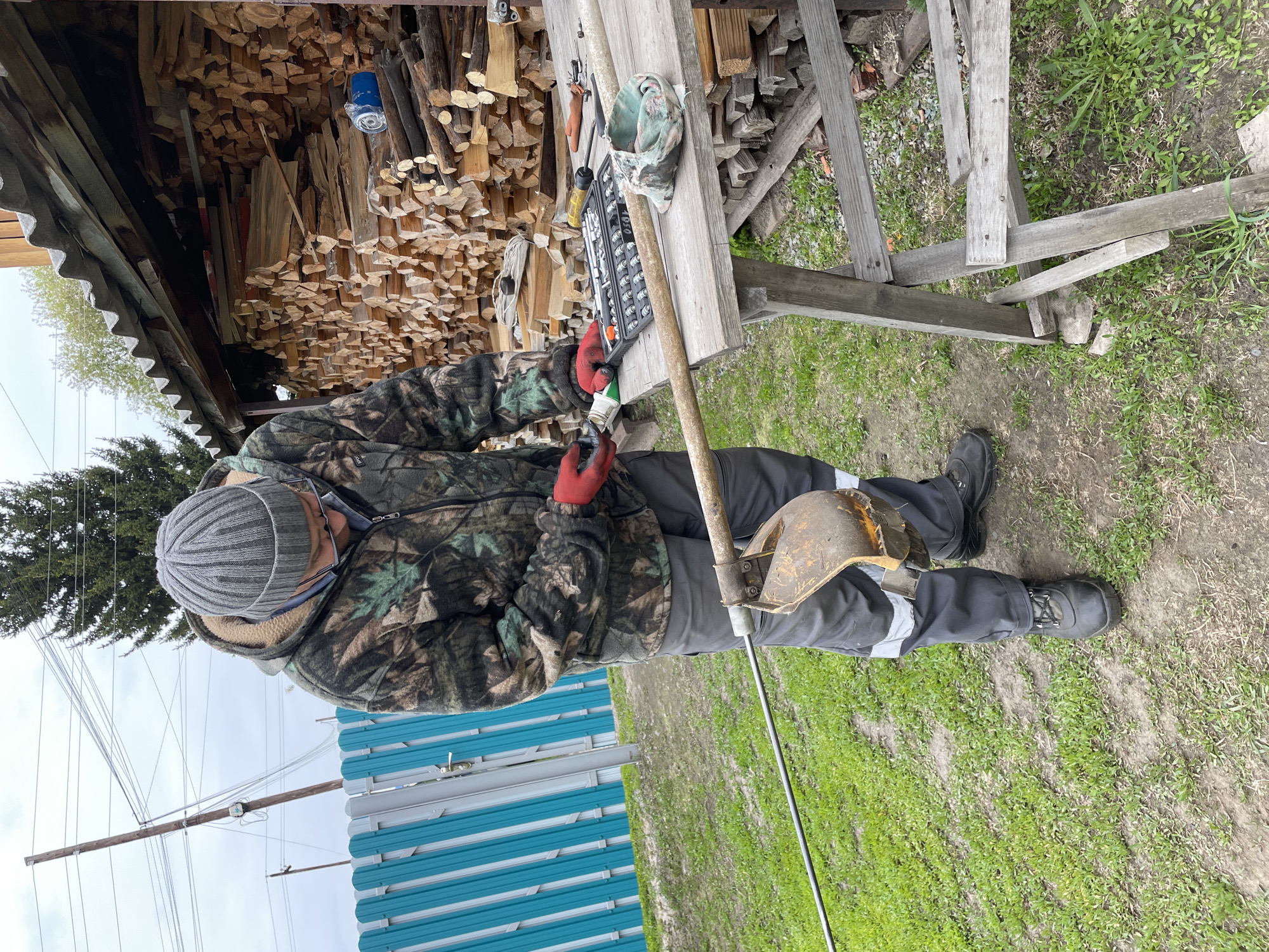 Man repairs weed whacker in outdoor workshop, Talmenka Russia