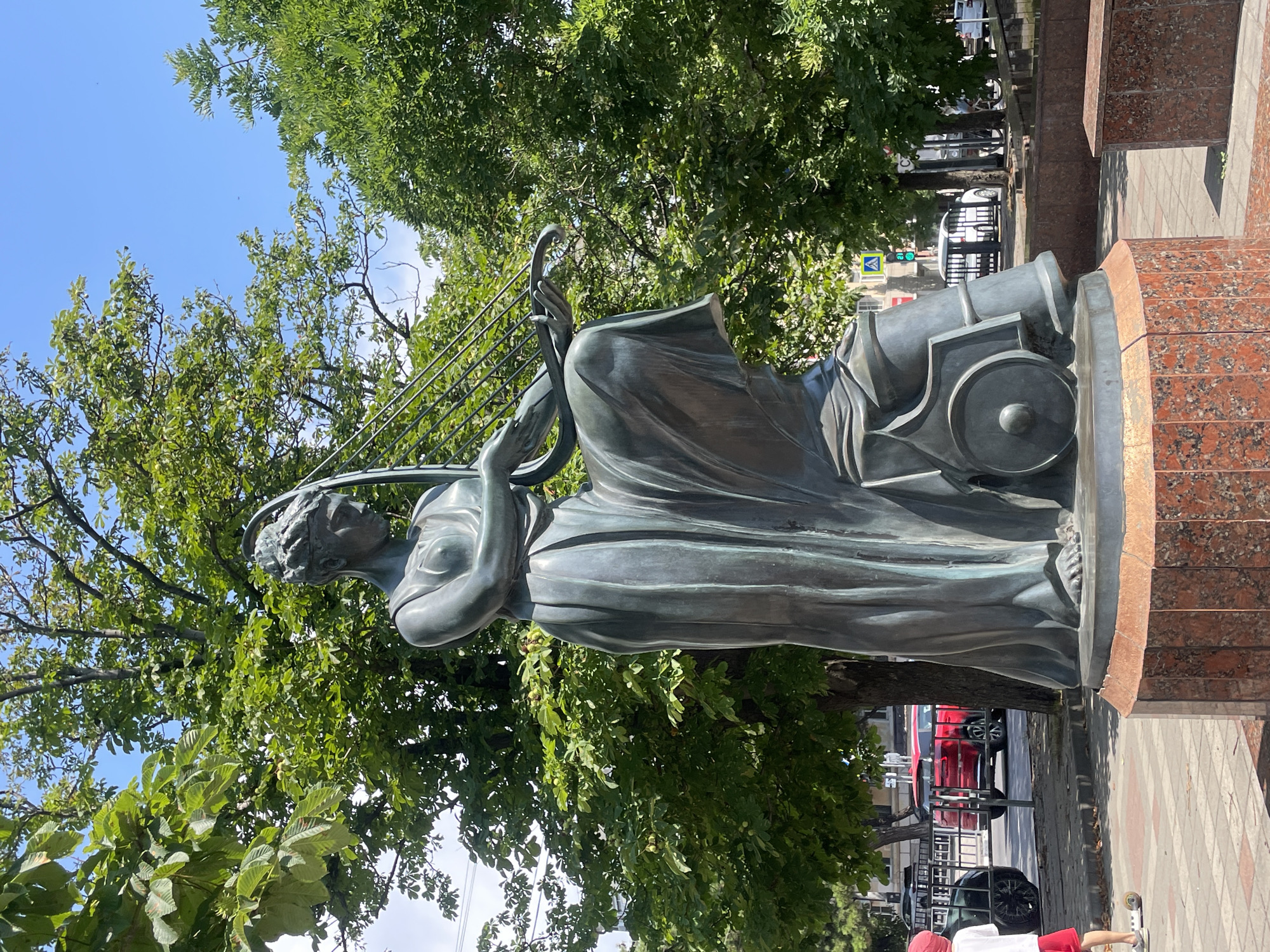 Bronze lyre-playing statue on a red granite pedestal