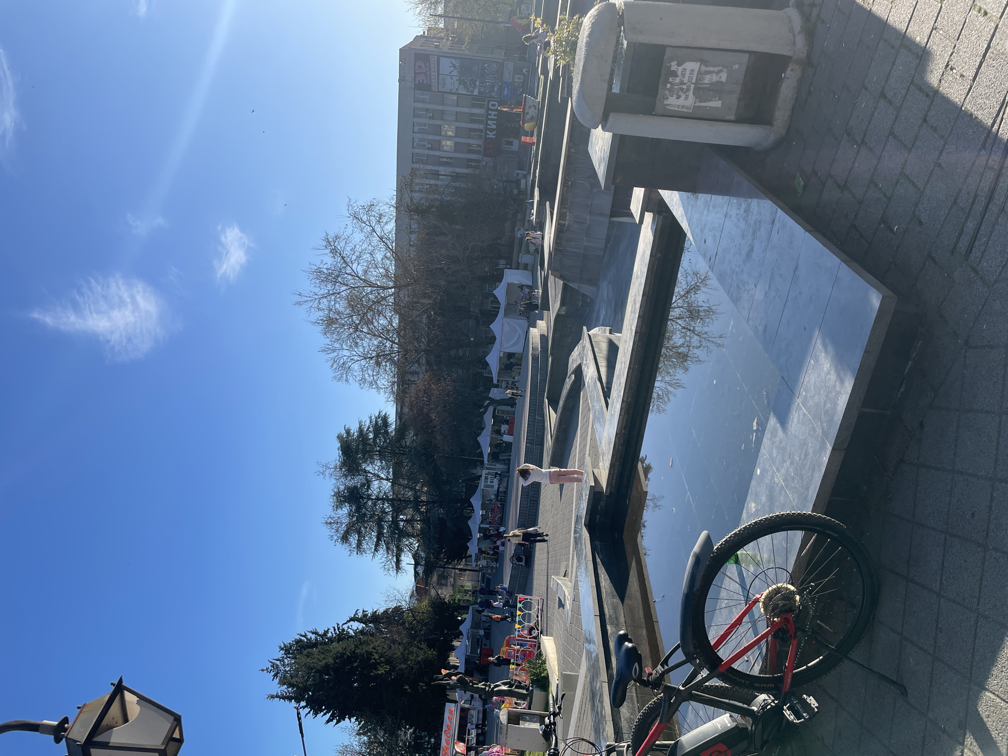 Dog rests in sunny Pazardzhik plaza alongside parked bicycle