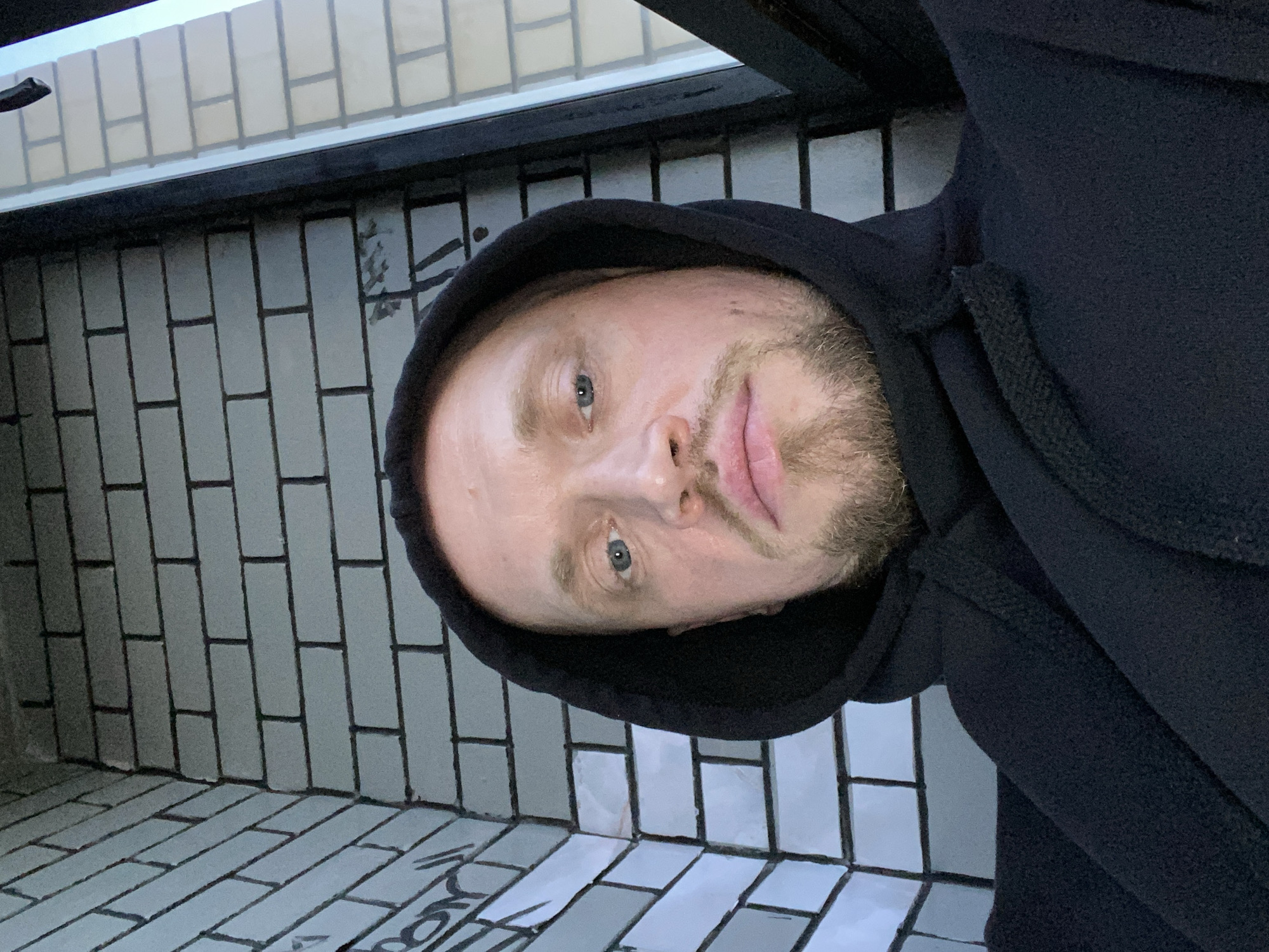 Overhead selfie in a black hoodie against a brick wall