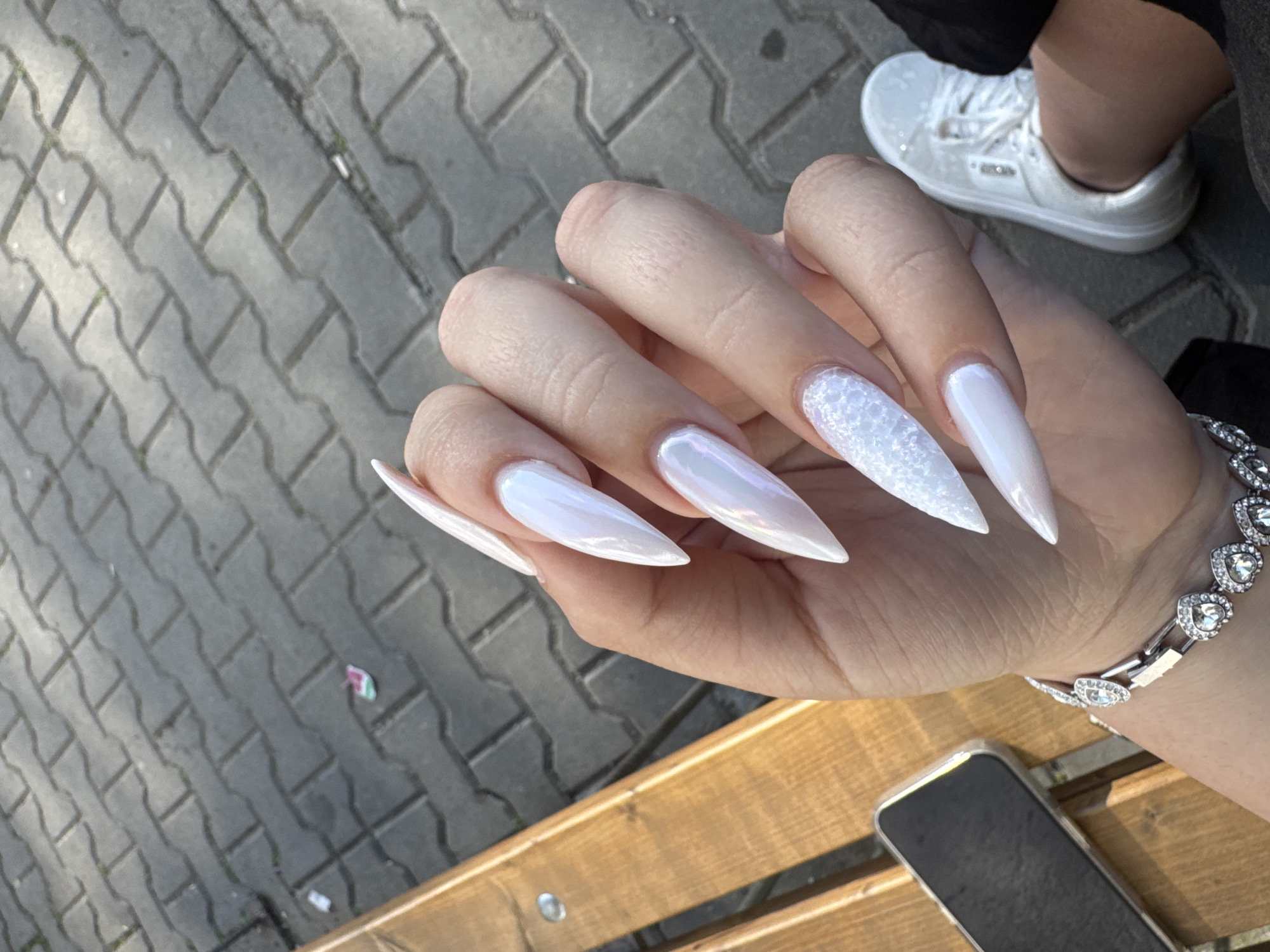 Person displays elaborate white stiletto nails with glitter finish