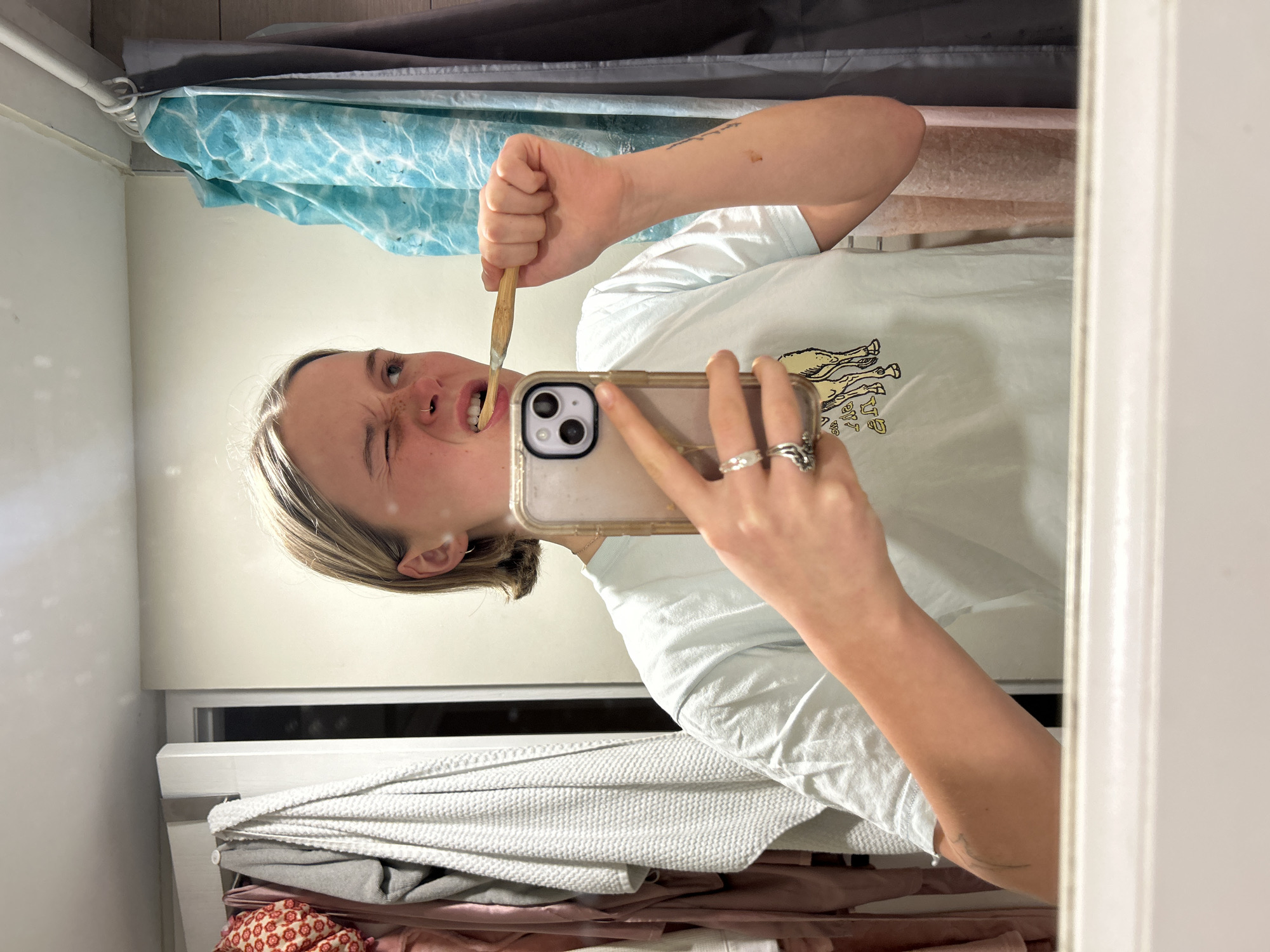 Person takes bathroom mirror selfie while brushing teeth