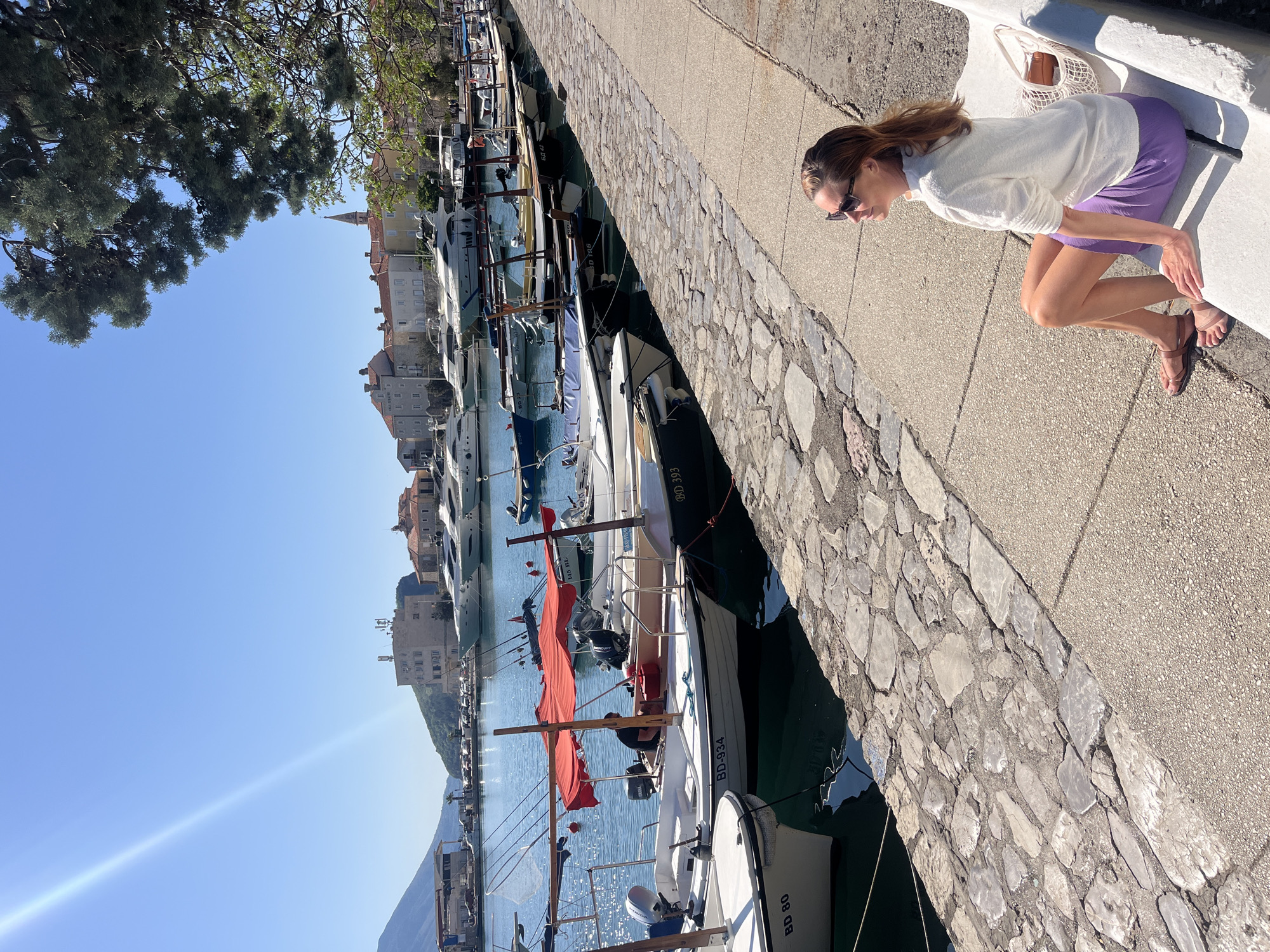 Woman in purple skirt strolls Budva waterfront, watches boats and ducks