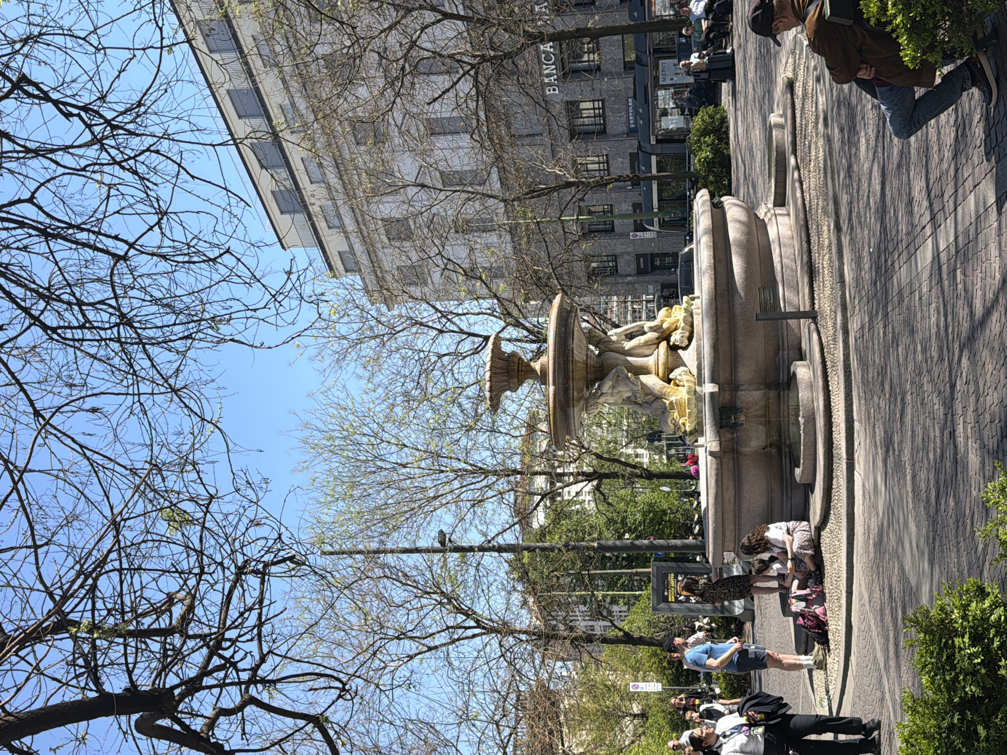 Crowds gather around historic stone fountain in Milan