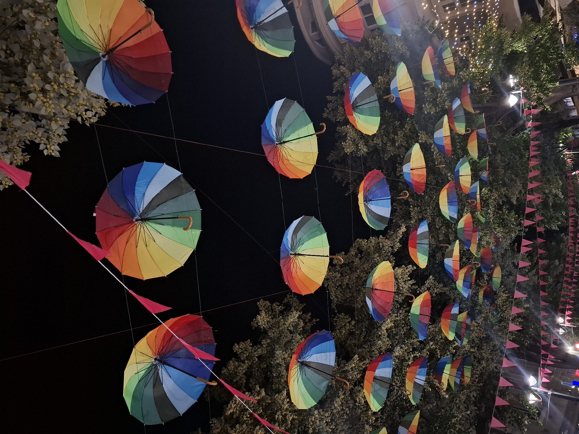Rainbow umbrellas hang over a lit-up street at night