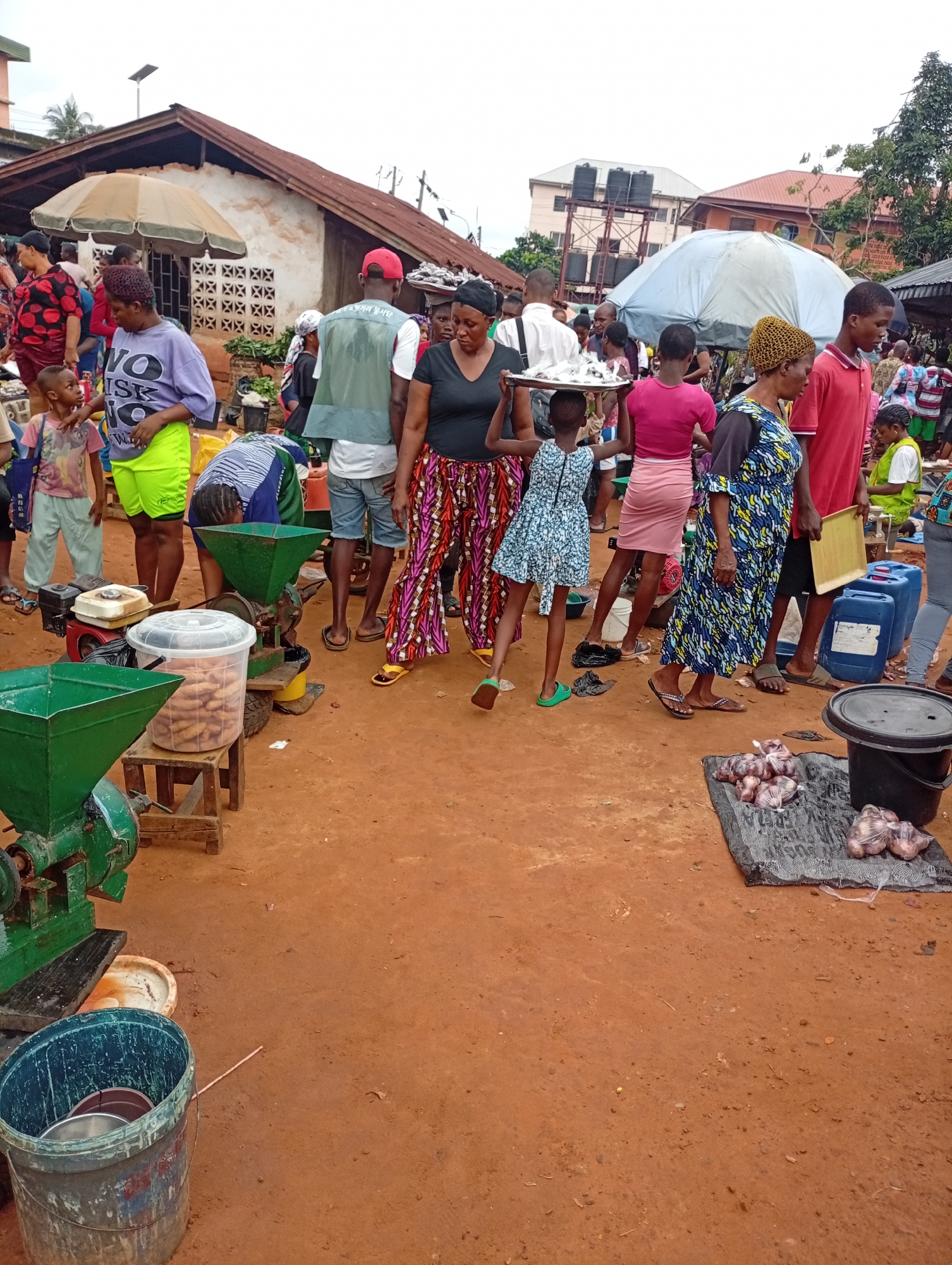 Busy outdoor market on red dirt ground, midmorning.