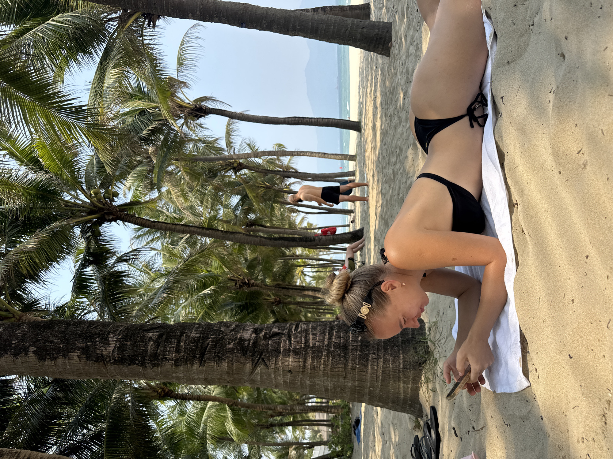 Woman relaxes on phone at palm-lined Đà Nẵng beach