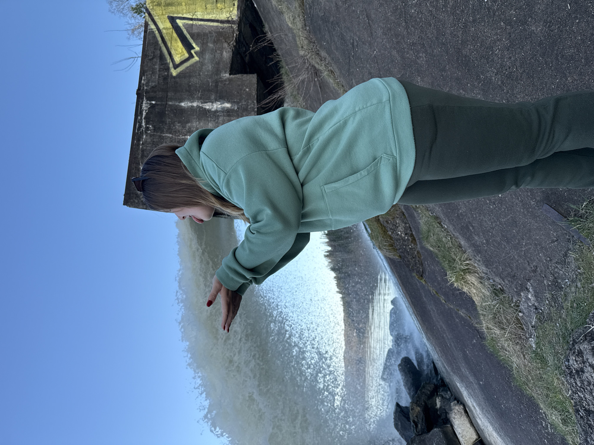 Woman reaches toward waterfall at concrete structure in Russia