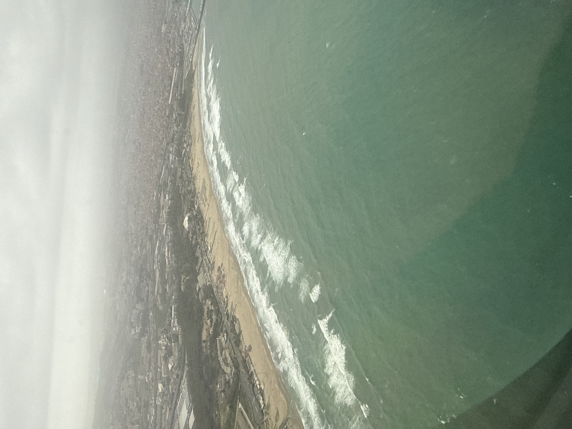 Aerial view captures Catania coastline with waves and cityscape