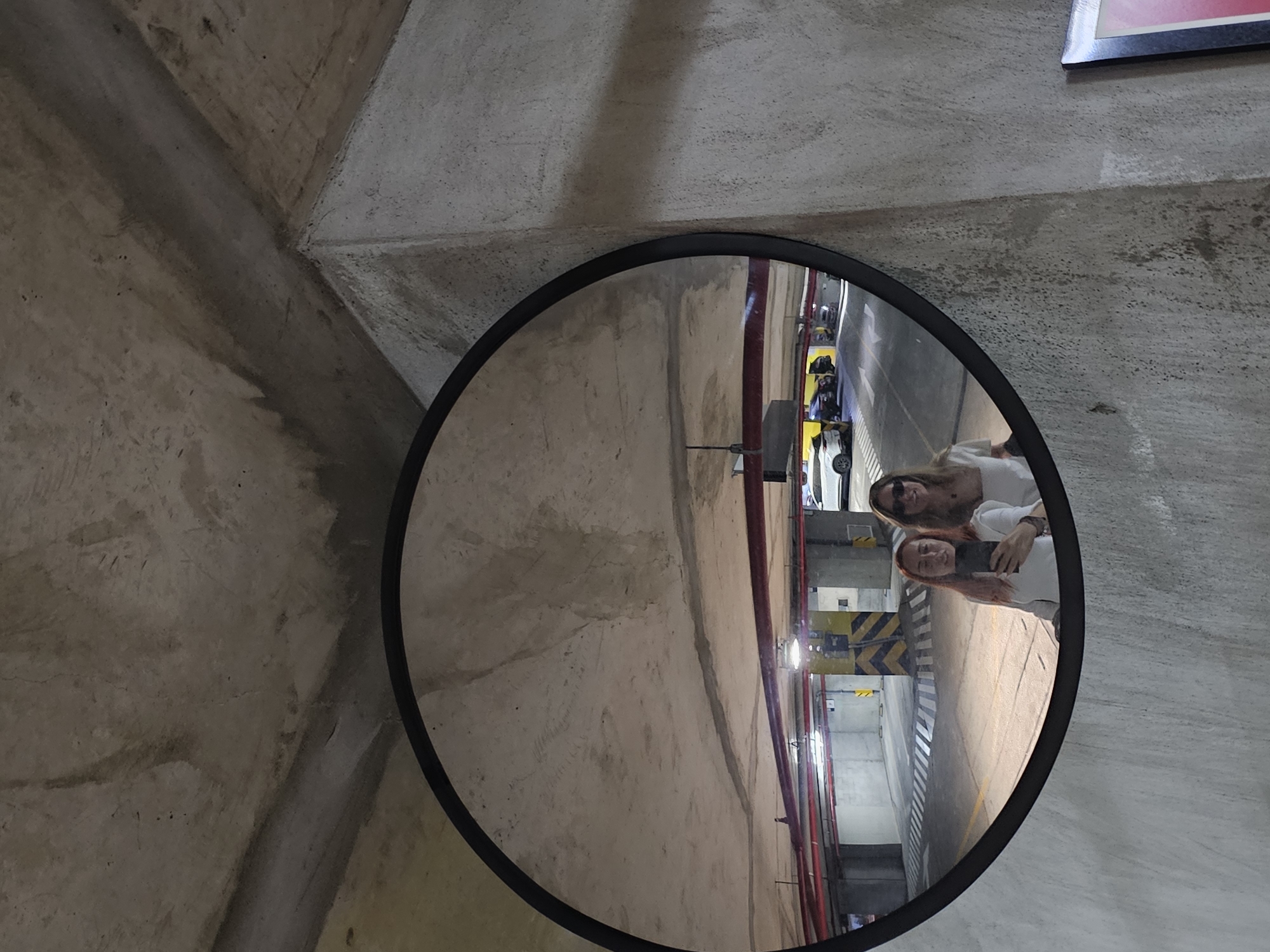Security mirror reflects parking garage view on concrete wall