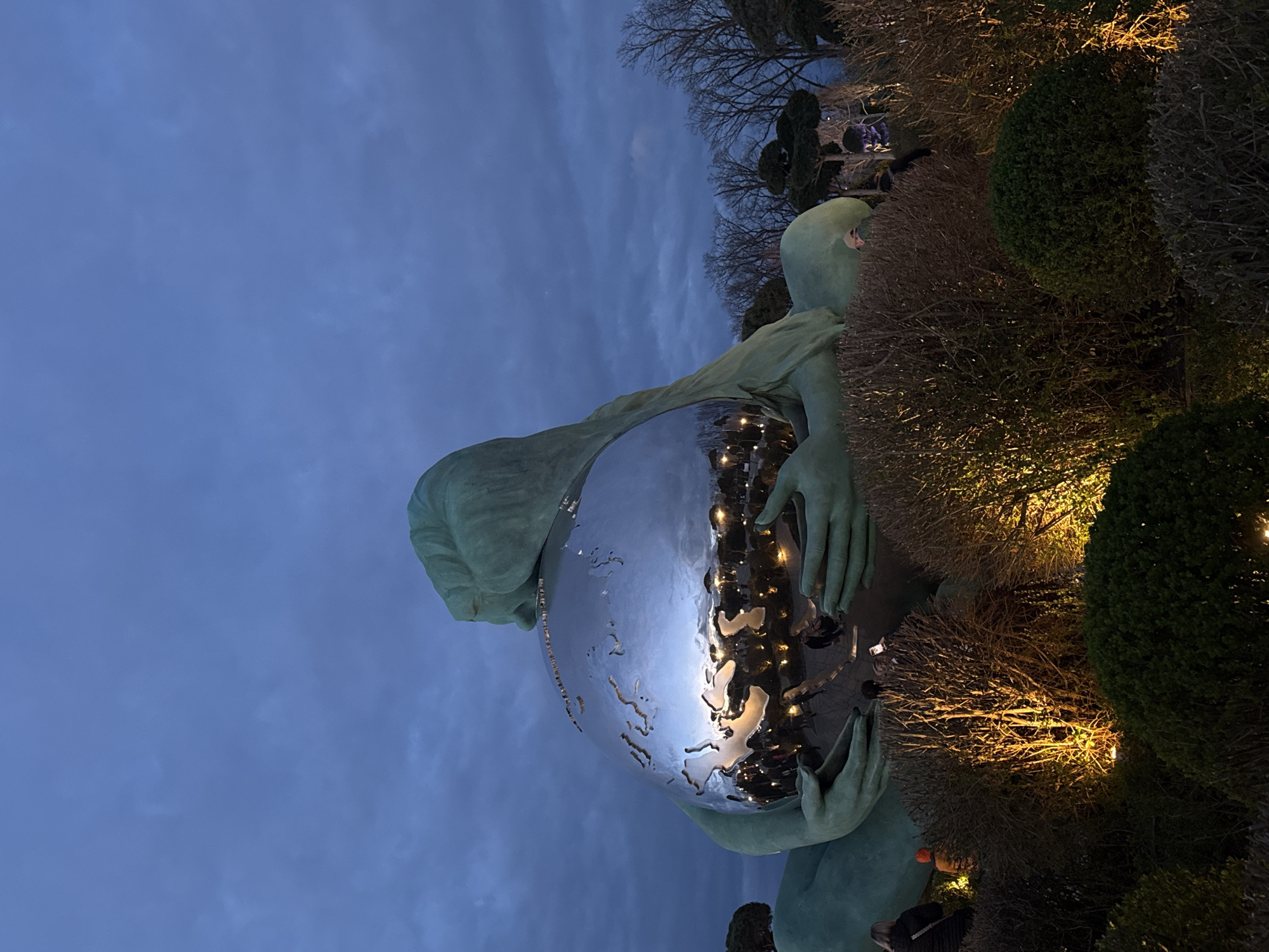 Evening park scene with illuminated statue and light-adorned trees