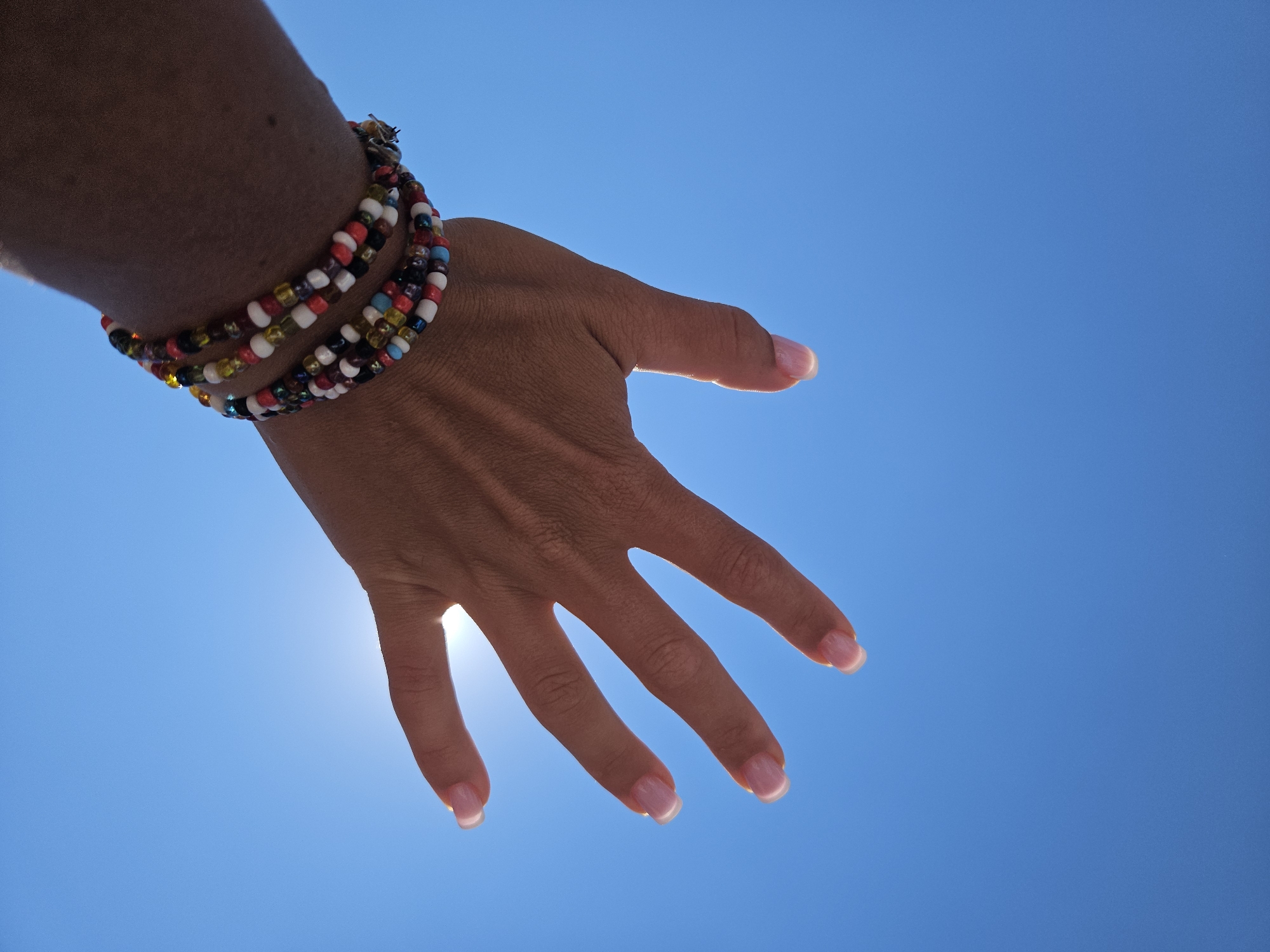 Beaded bracelets raised against a sun-flared blue sky