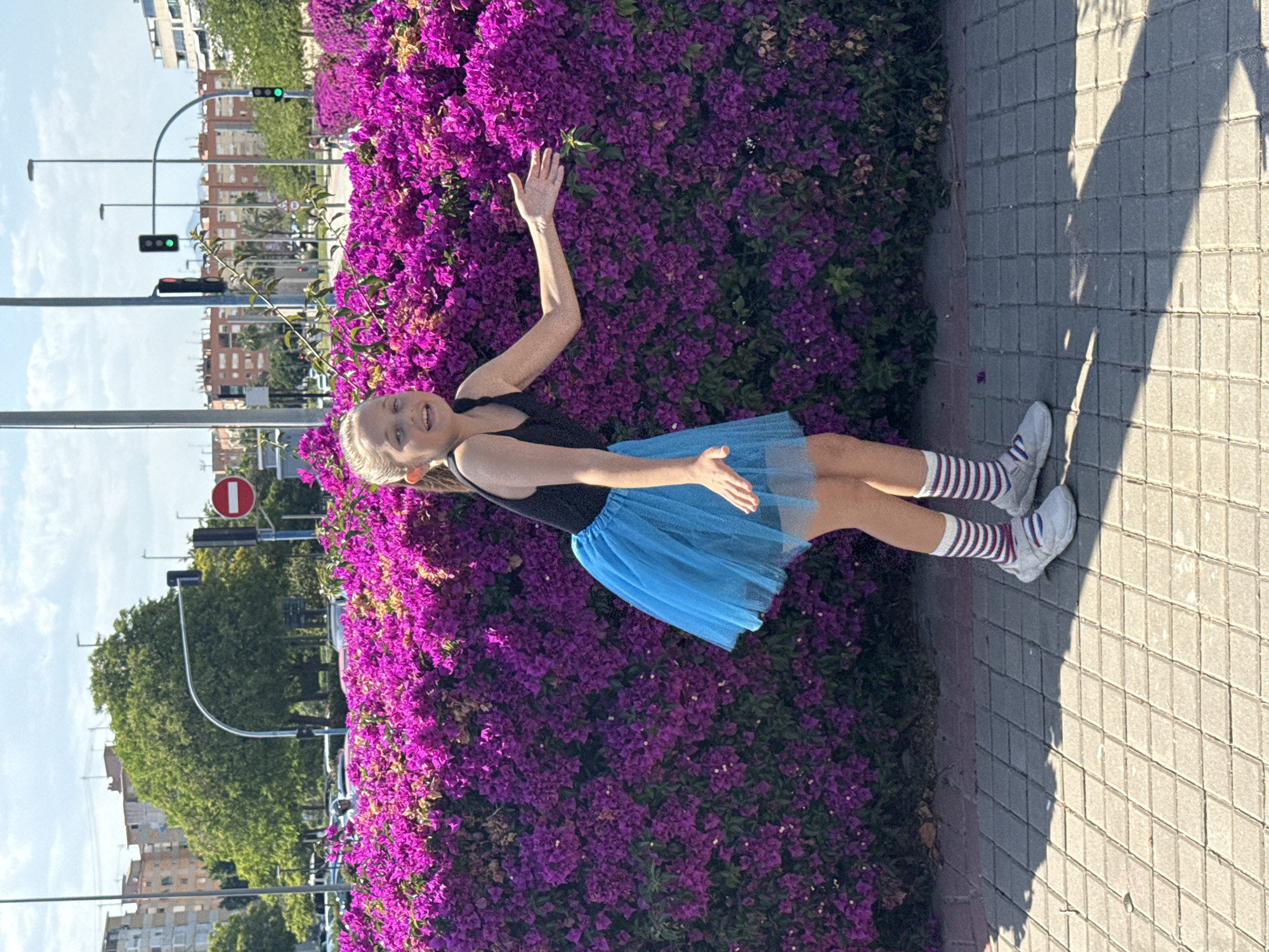 Girl in blue tutu photographed near purple flowers, urban setting