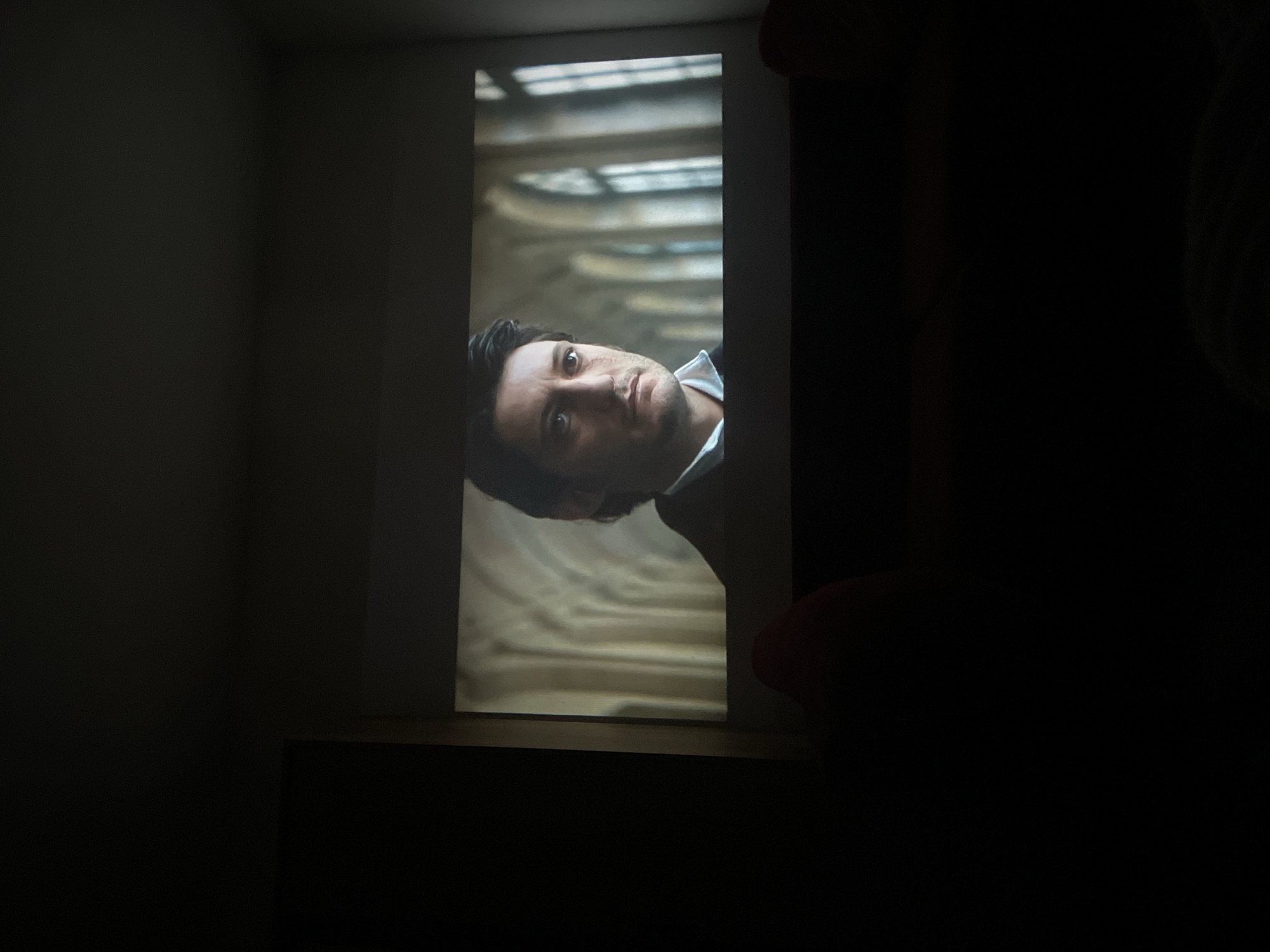 Man's image displayed on screen in darkened Murino room