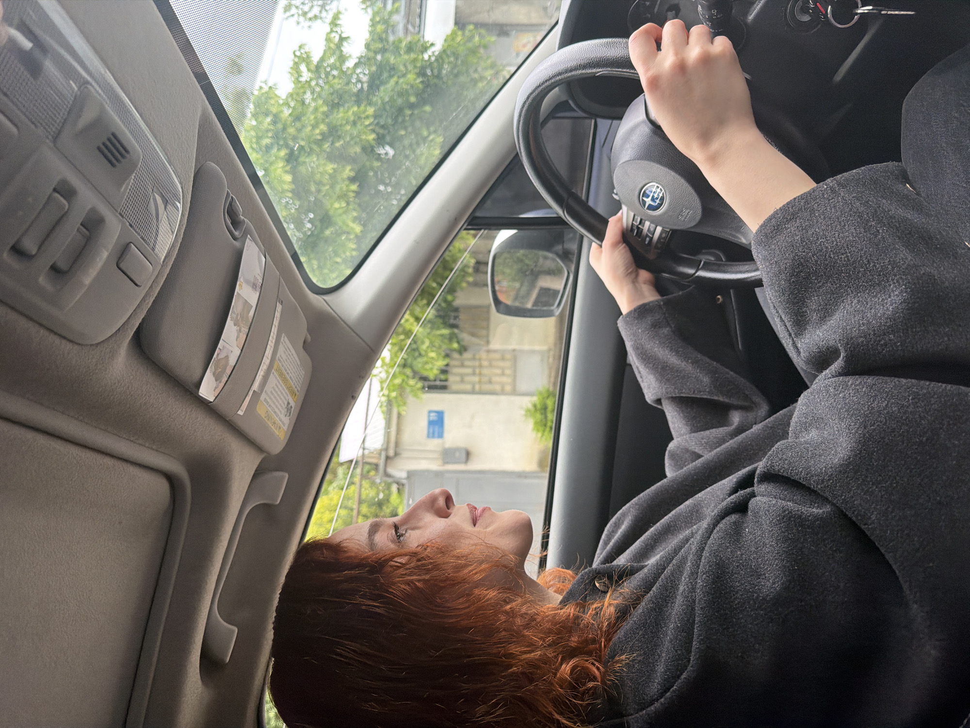 Woman drives Subaru through green hills of Tbilisi morning