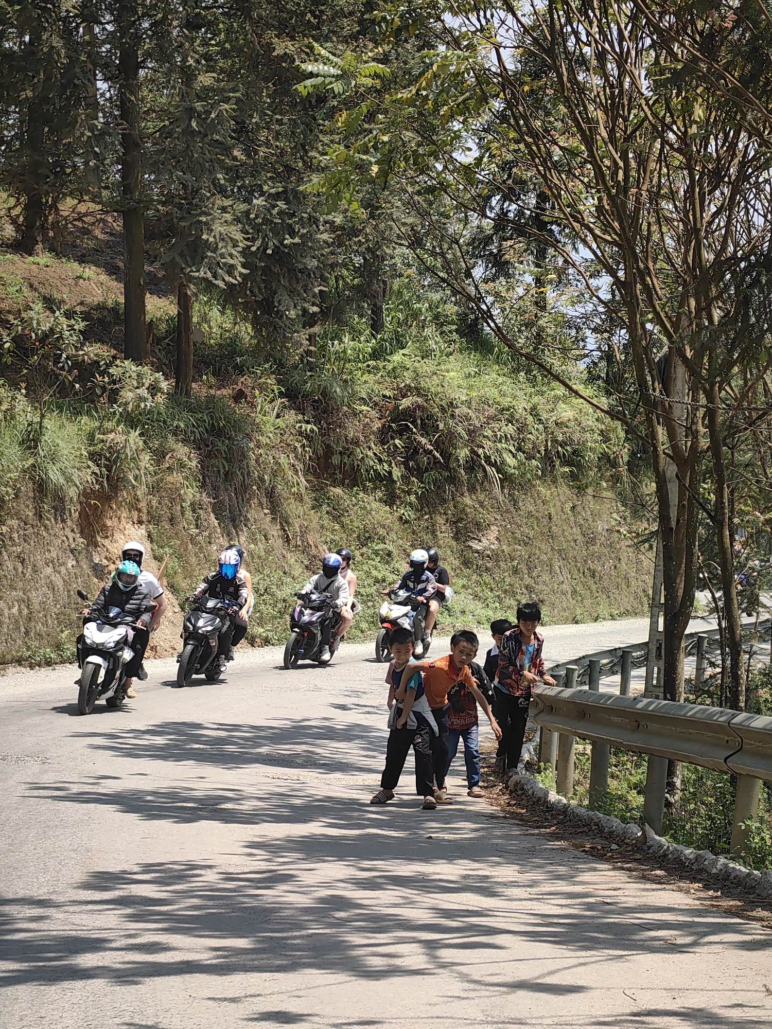 Motorcyclists travel mountain road past children in Vietnam commune