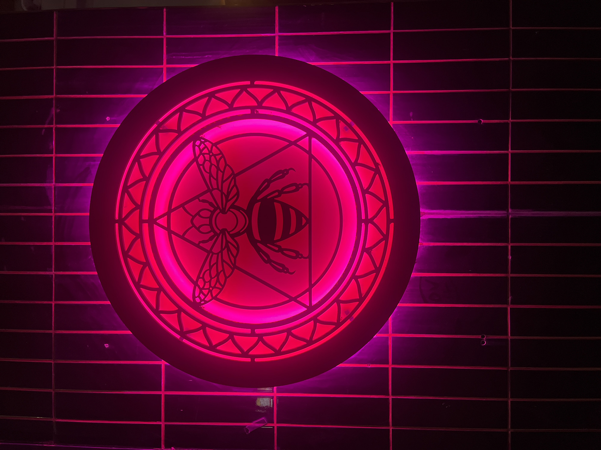 Pink neon bee sign spotted on dark wall