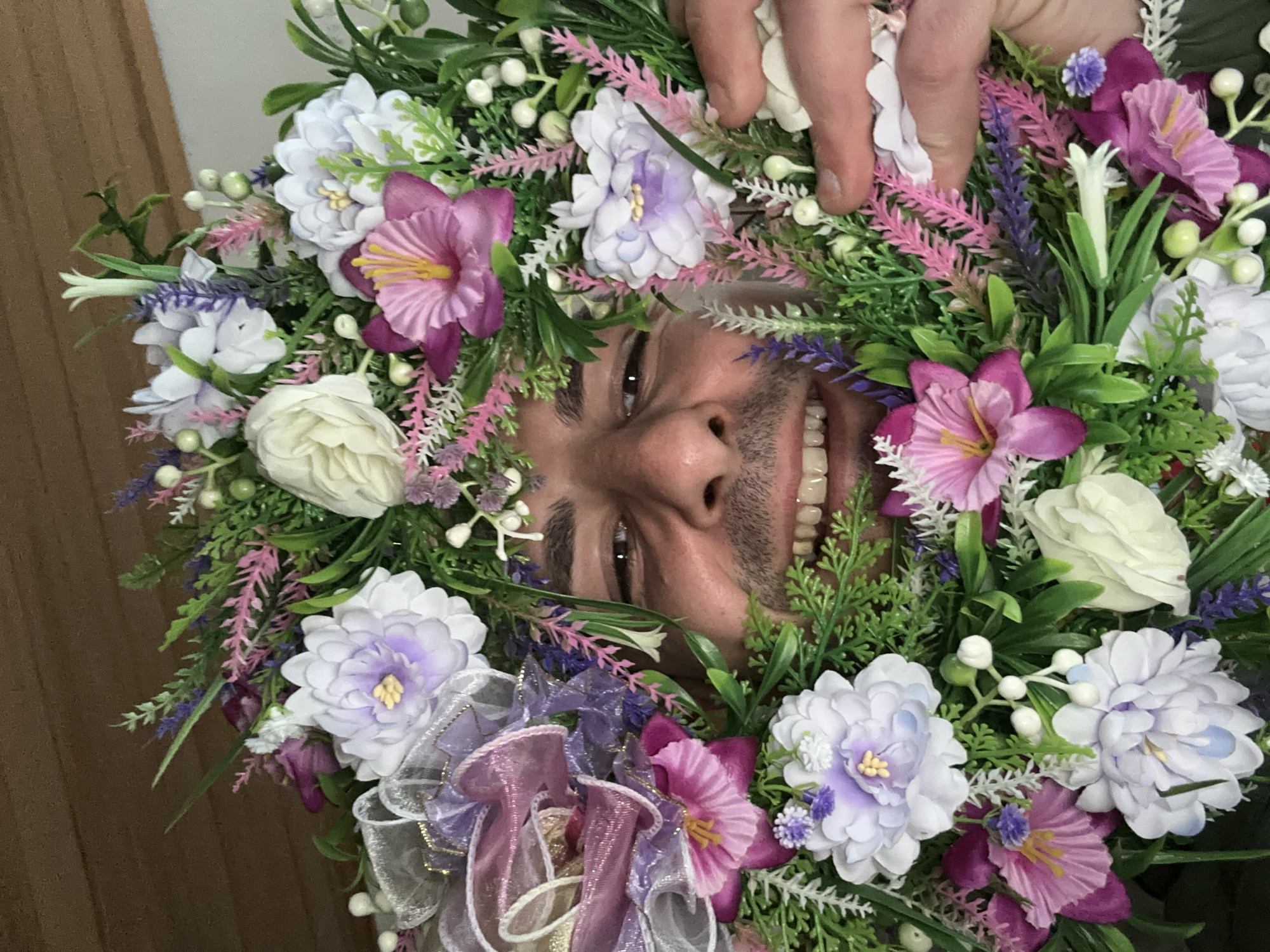 Man poses with floral wreath, candles displayed in Slavyani