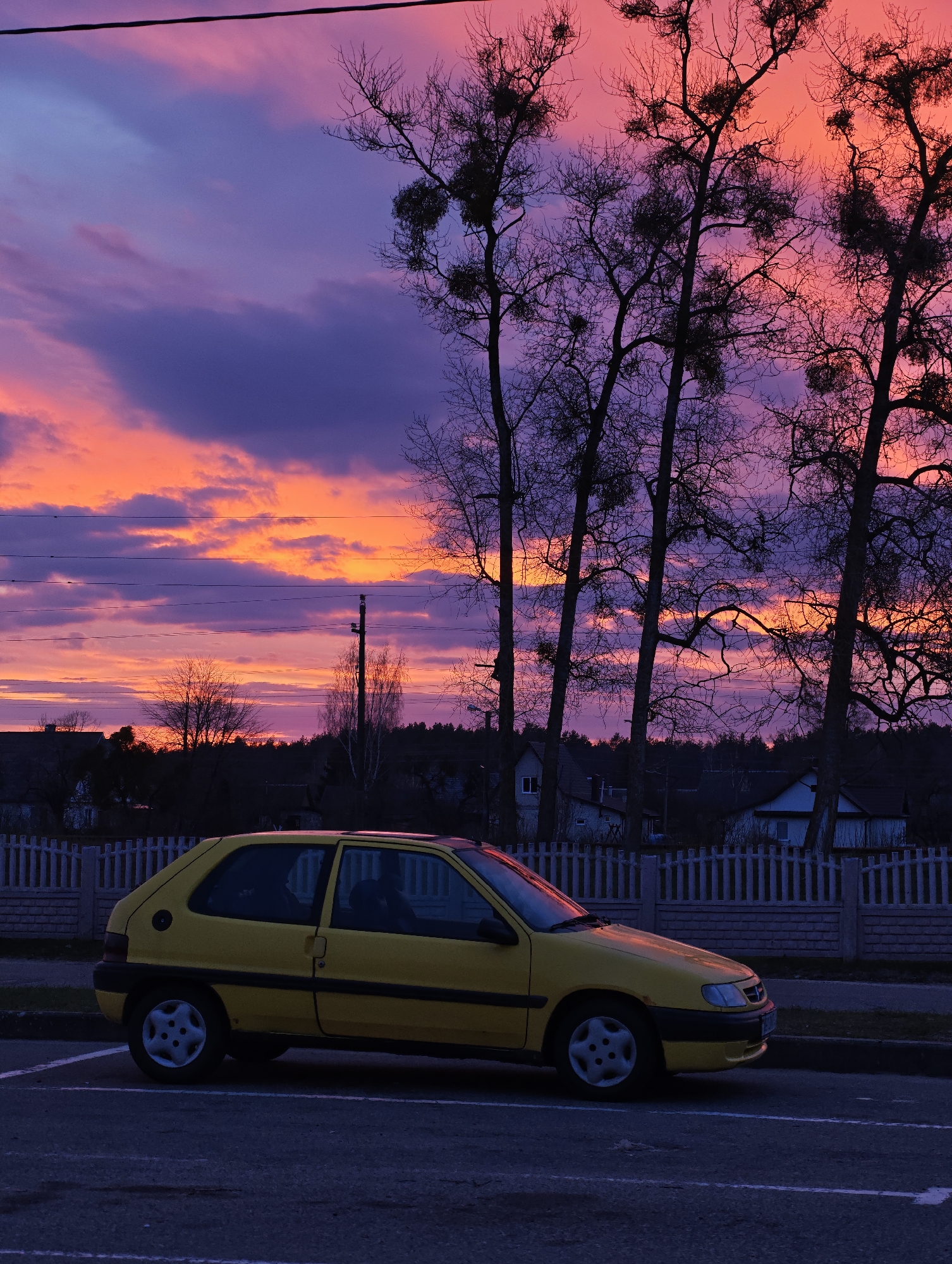 Yellow Citroen parked near residential fence under pink sky