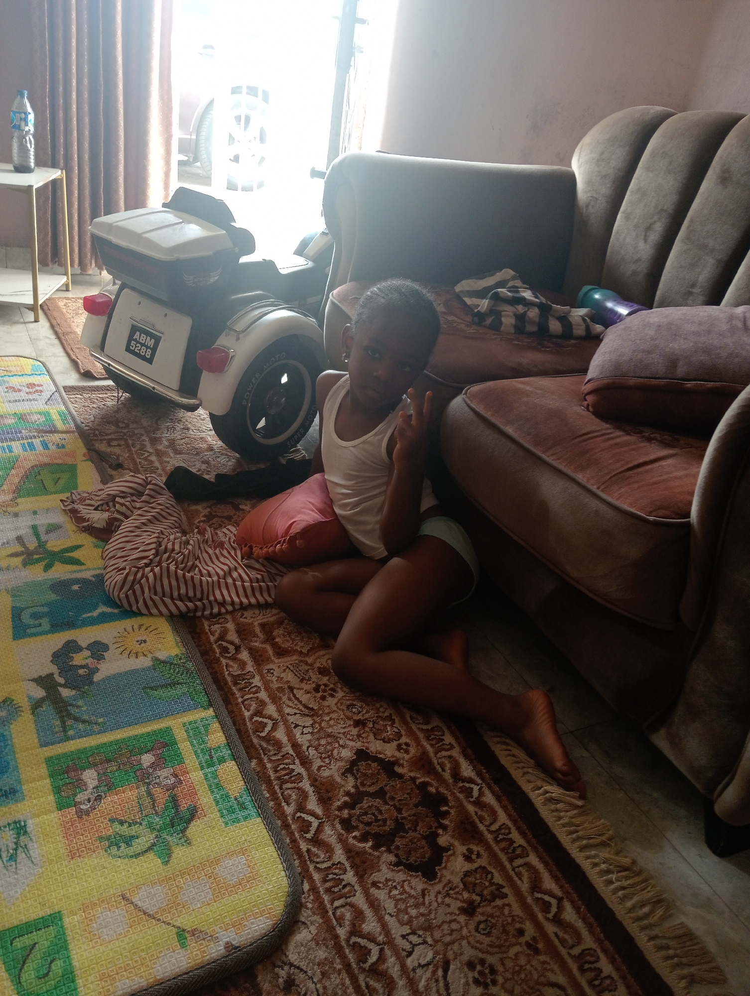 Child makes peace sign gesture on rug in Jos