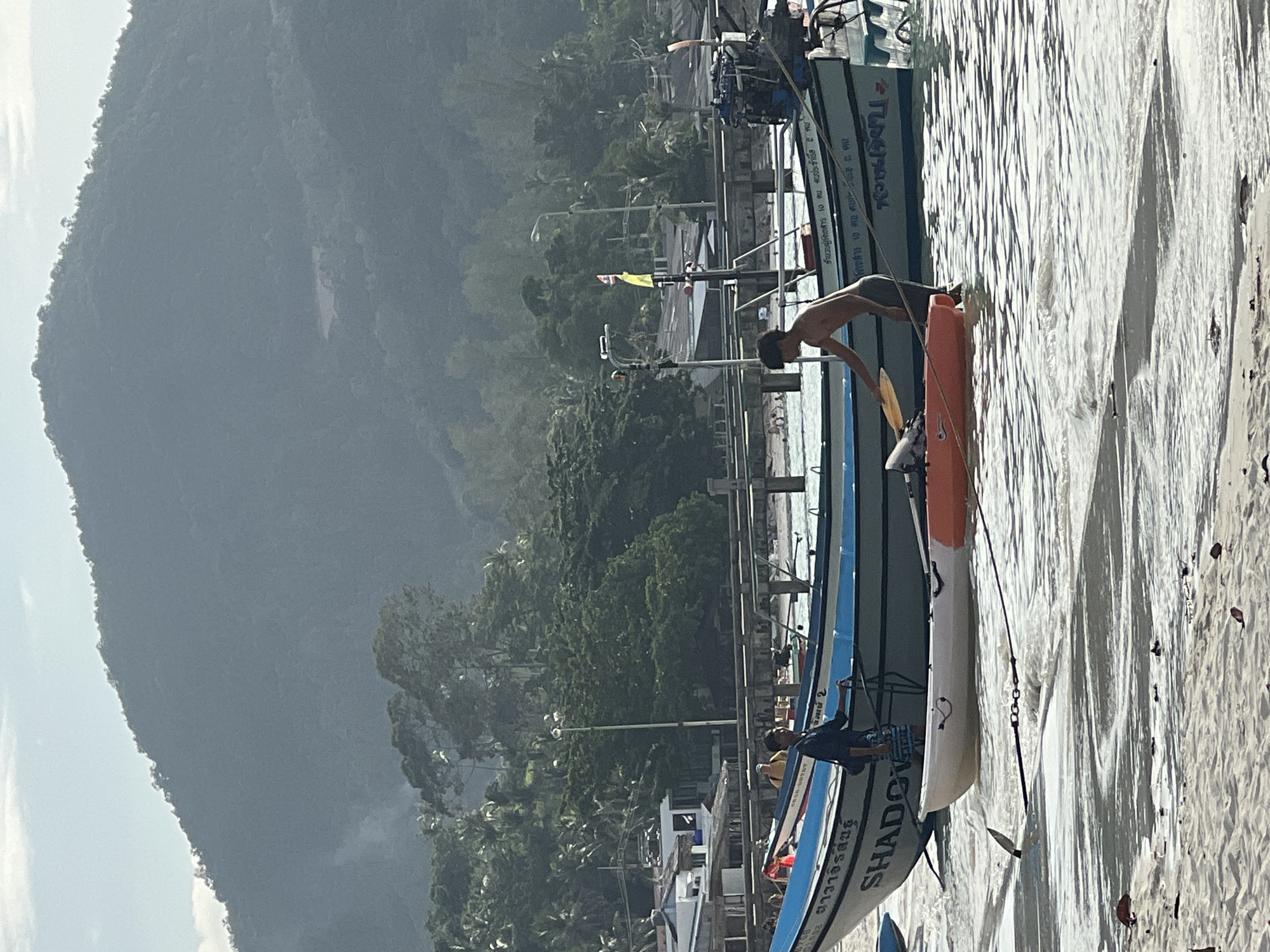 Longtail boats and beach activity at a shallow coastal anchorage