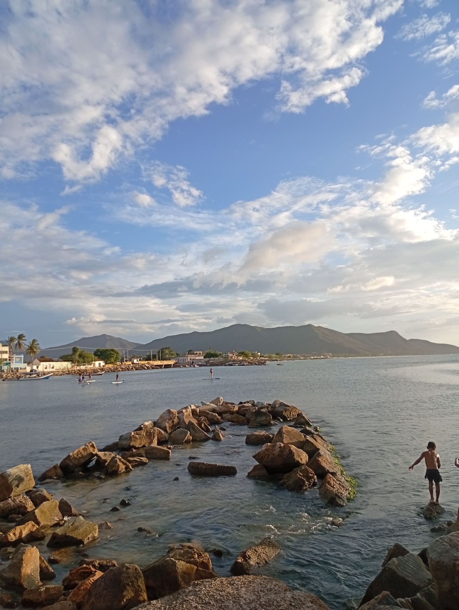 Rocky shoreline and beach at dusk, people in the water