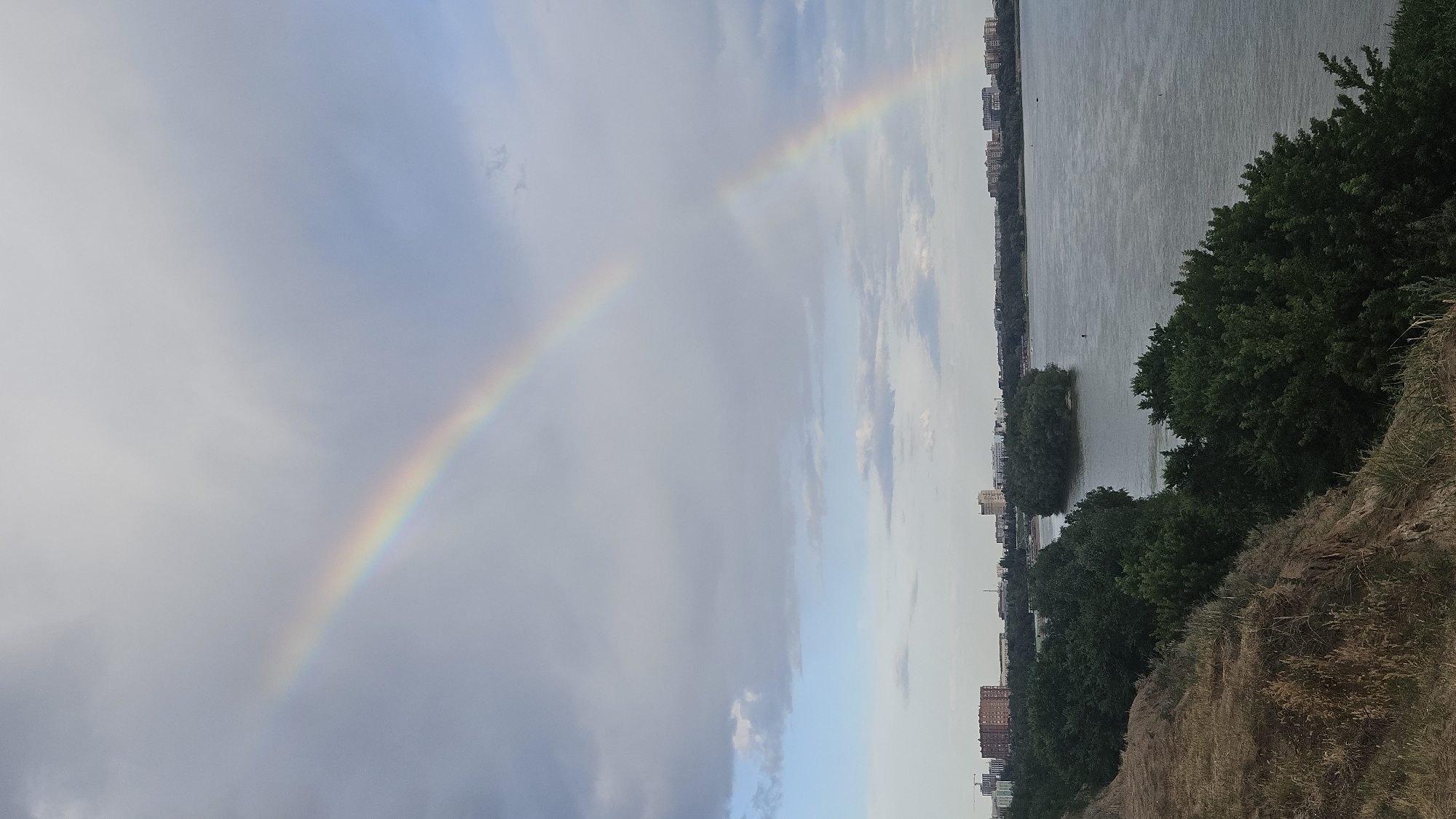 Rainbow over a wide river and metal bridge on a cloudy day