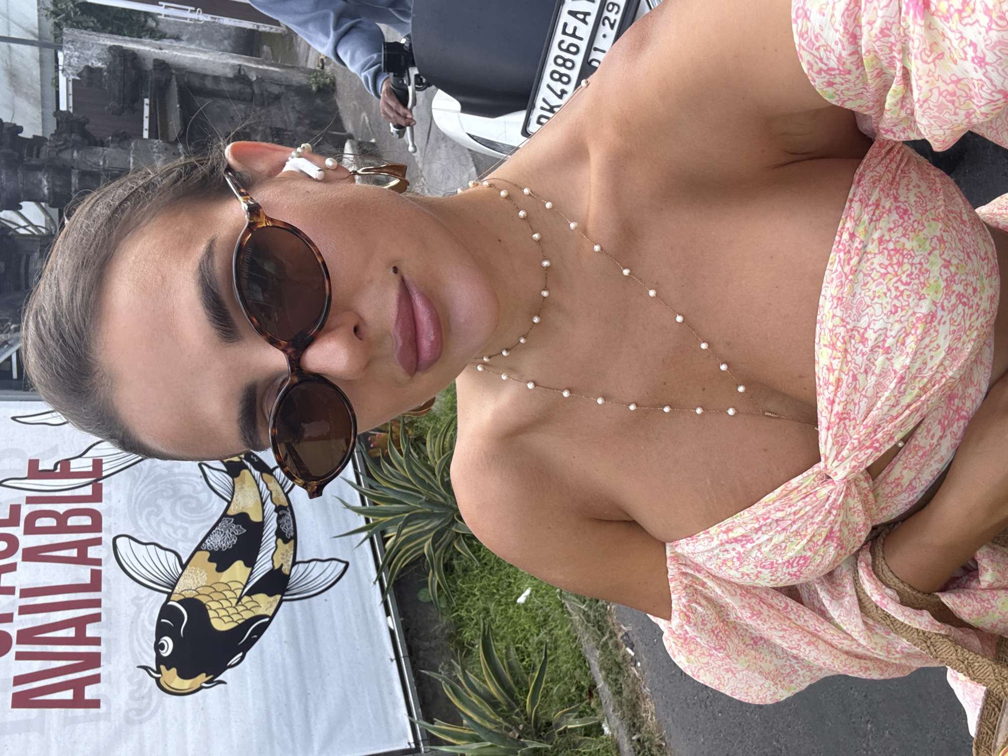 Woman in floral dress photographs herself, rides moped in Kuta