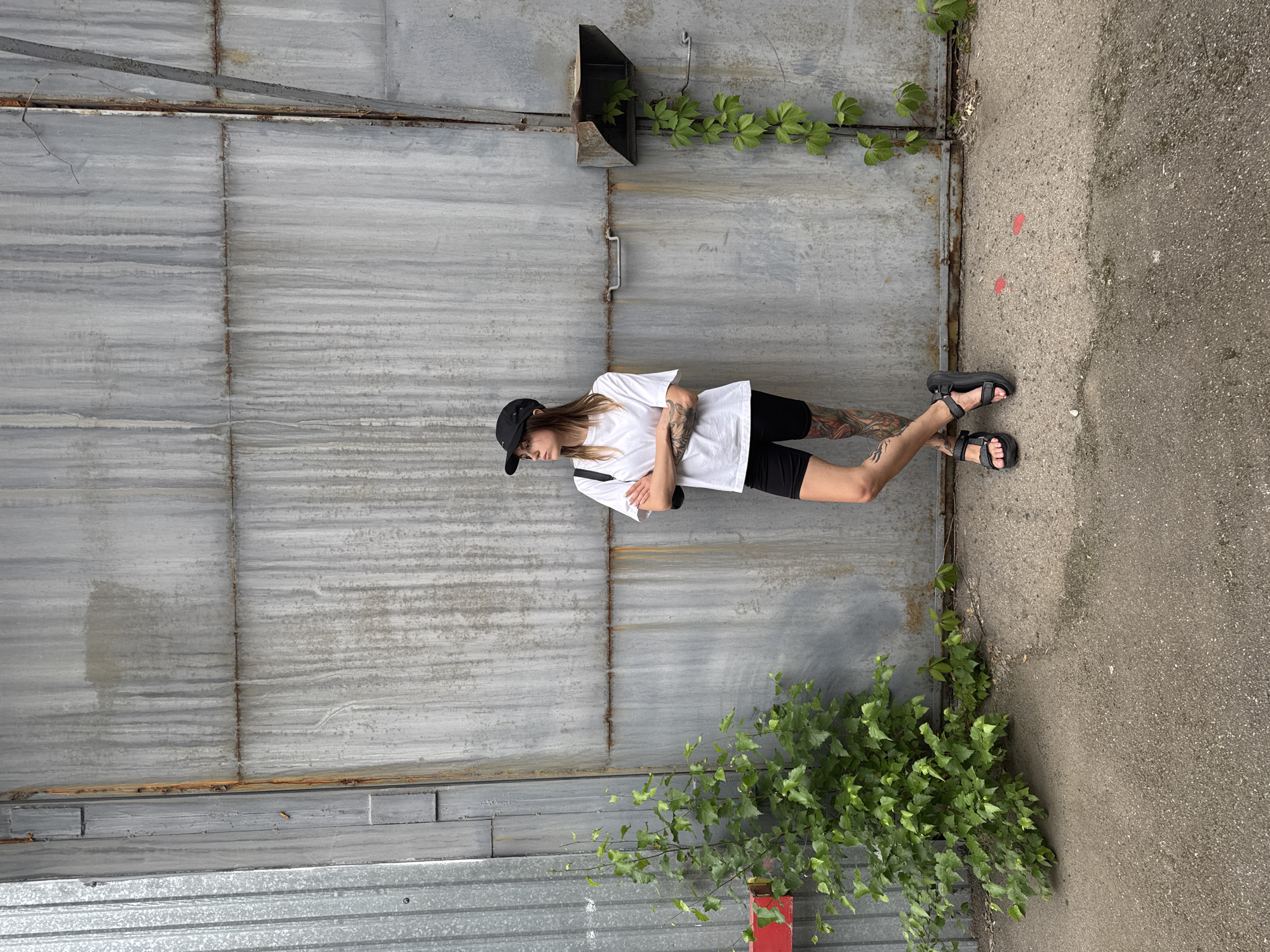 Tattooed figure poses against corrugated metal wall in Moscow