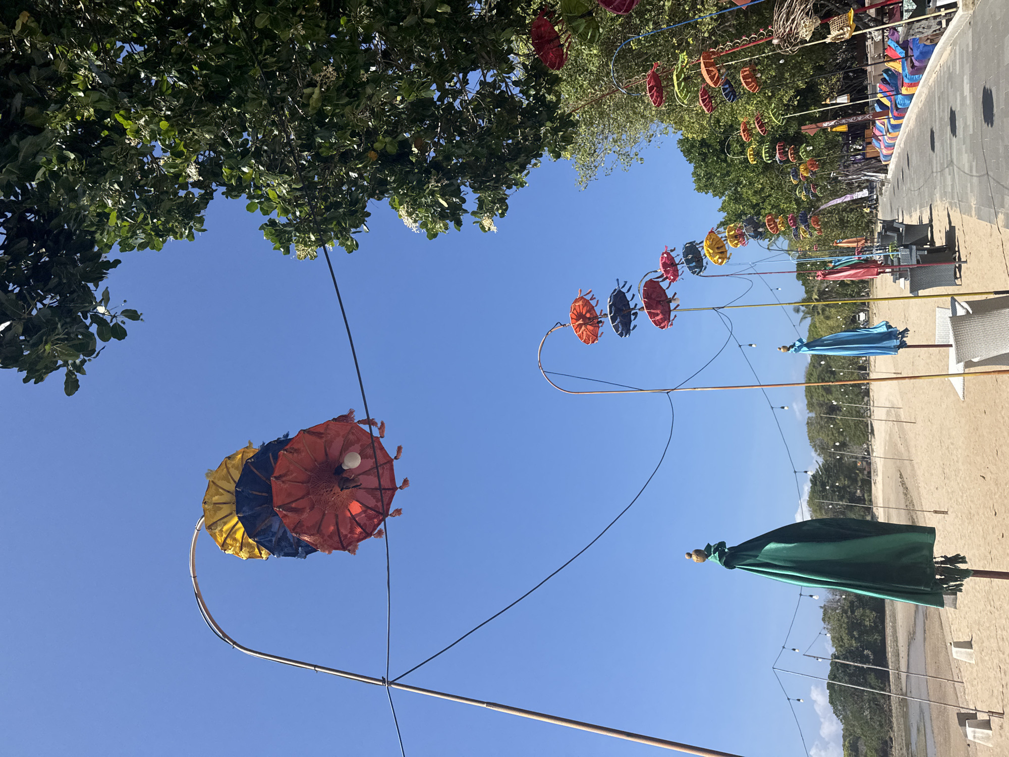 Colorful beachside promenade with kites, cyclists, and decorative umbrellas