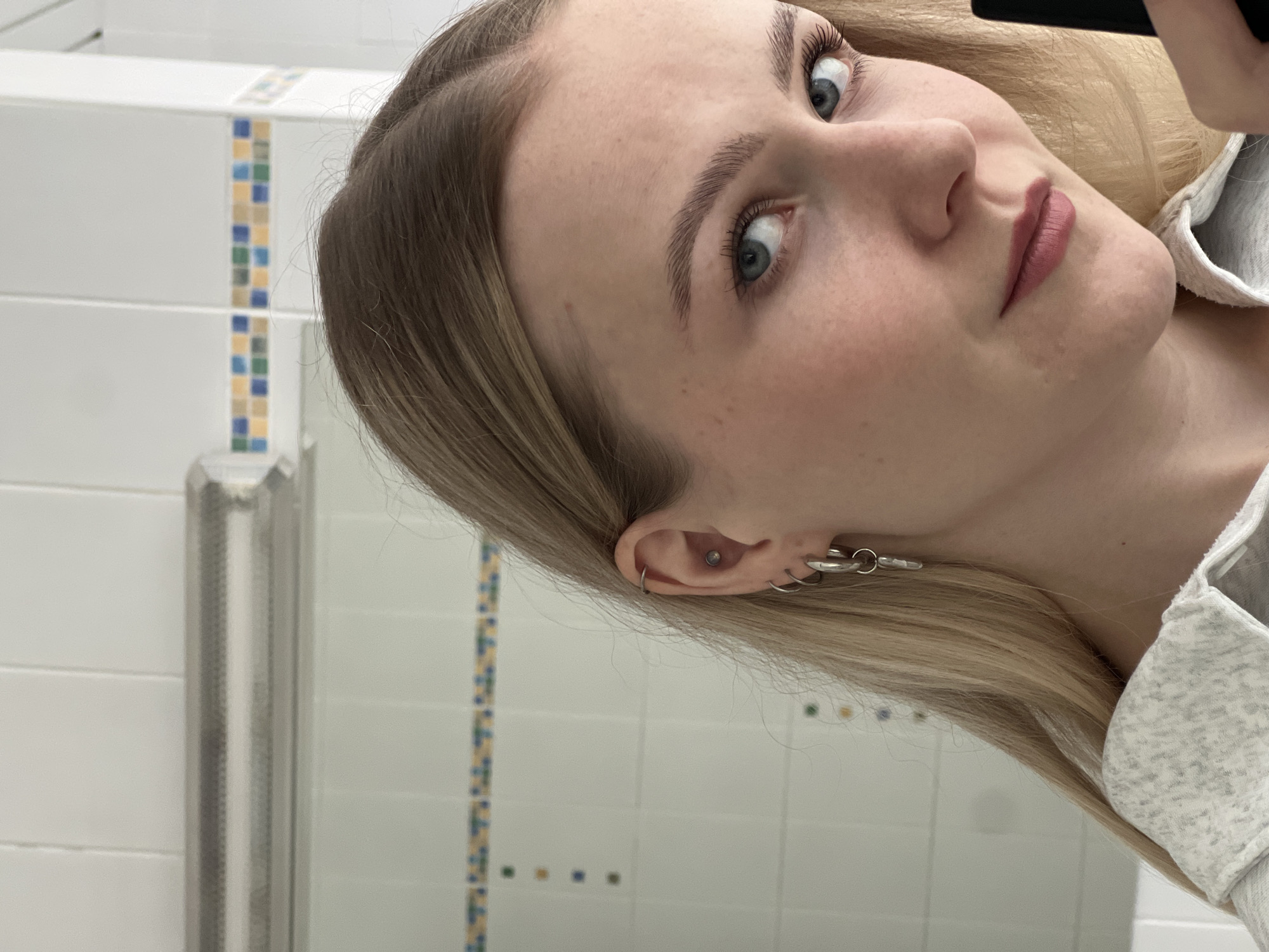 Woman takes mirror selfies in restroom wearing gray tracksuit