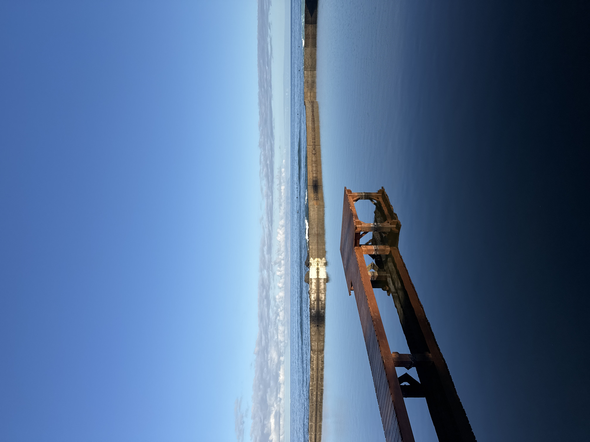 Tenerife coastline: pier, tidal pool, and surfers on a calm morning