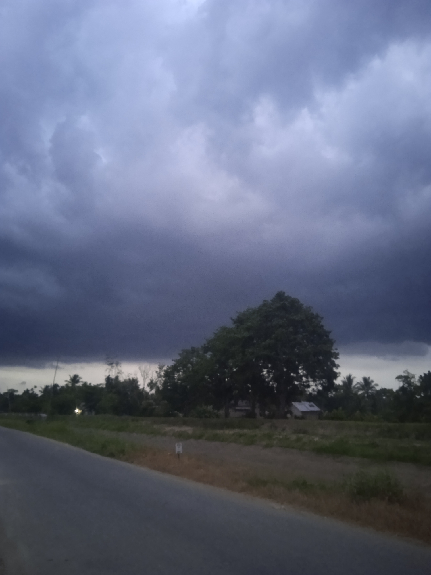 Storm clouds gathering over a quiet roadside stretch