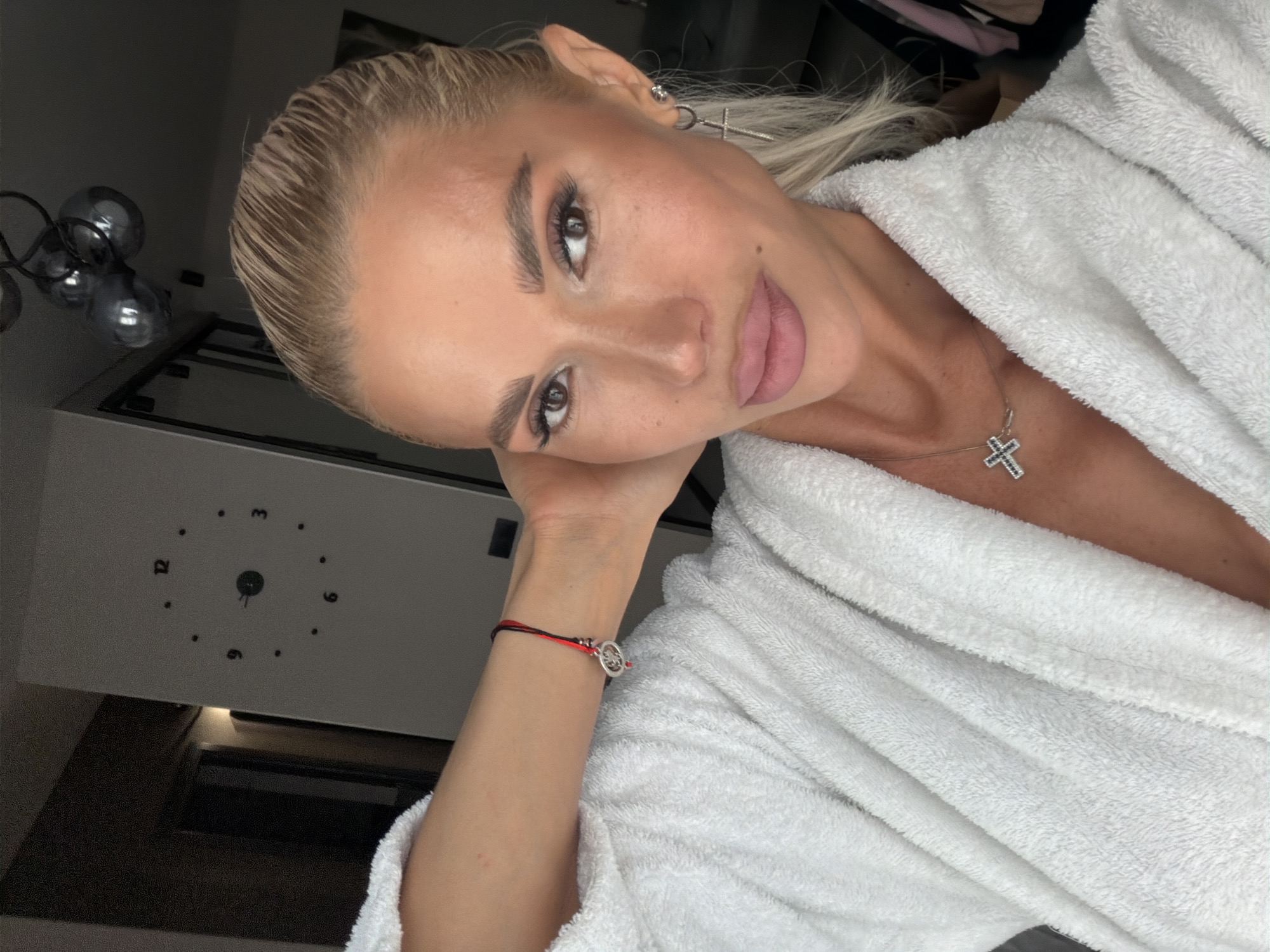 Woman takes selfie in bathrobe with cross jewelry