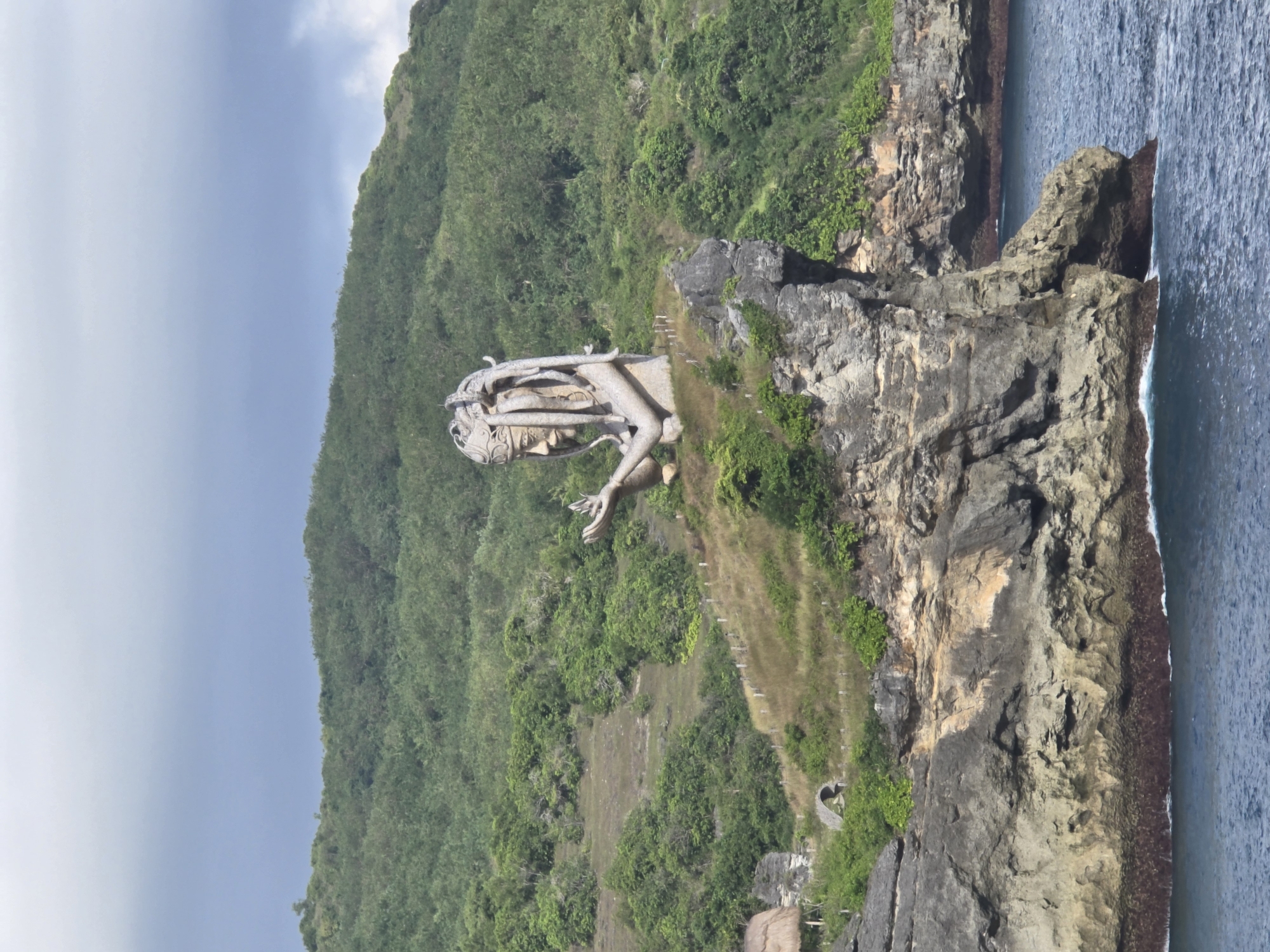 Stone deity sculpture spotted on ocean cliff in Nusa Penida