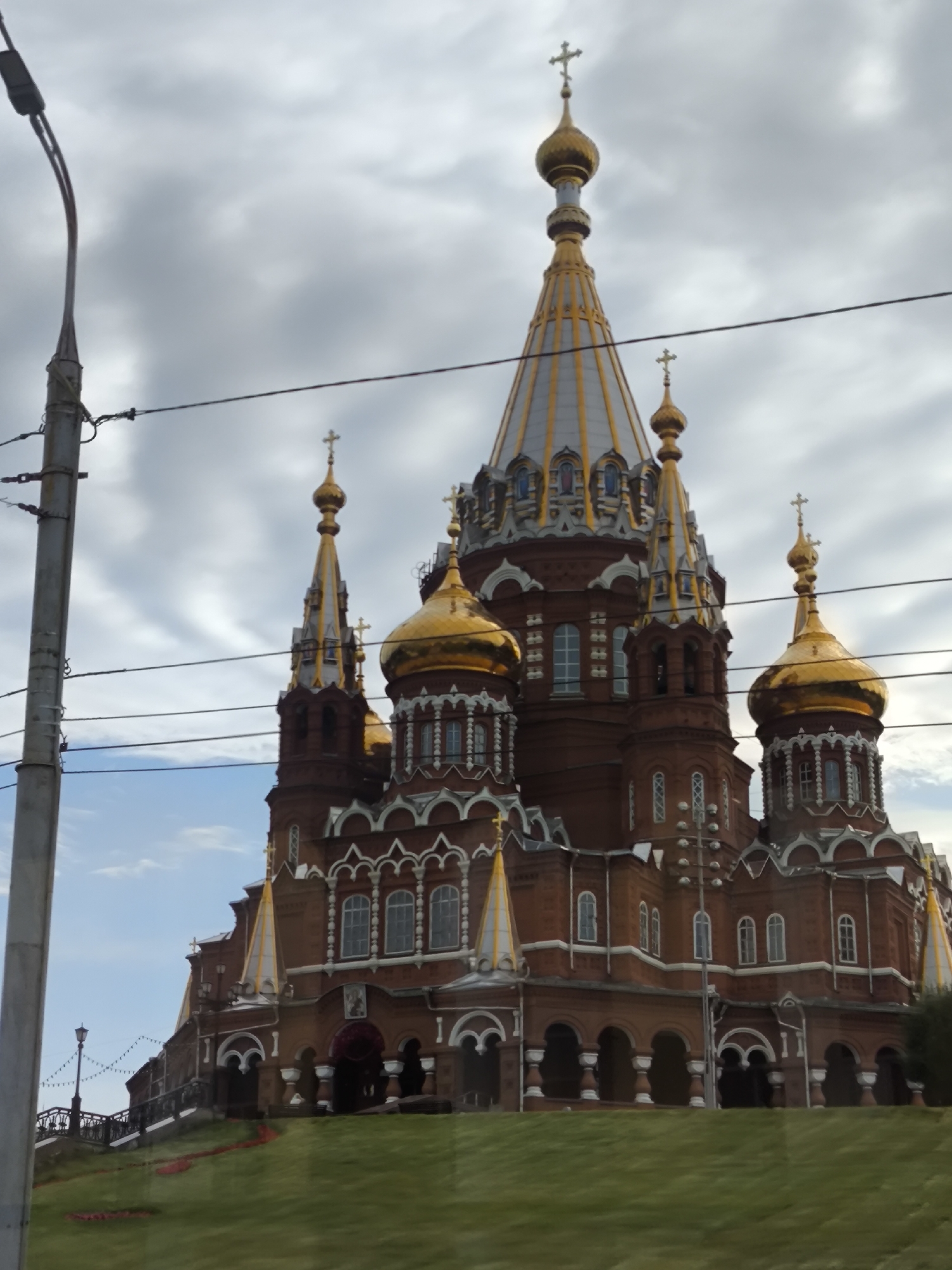 Ornate red brick cathedral with golden domes under cloudy skies